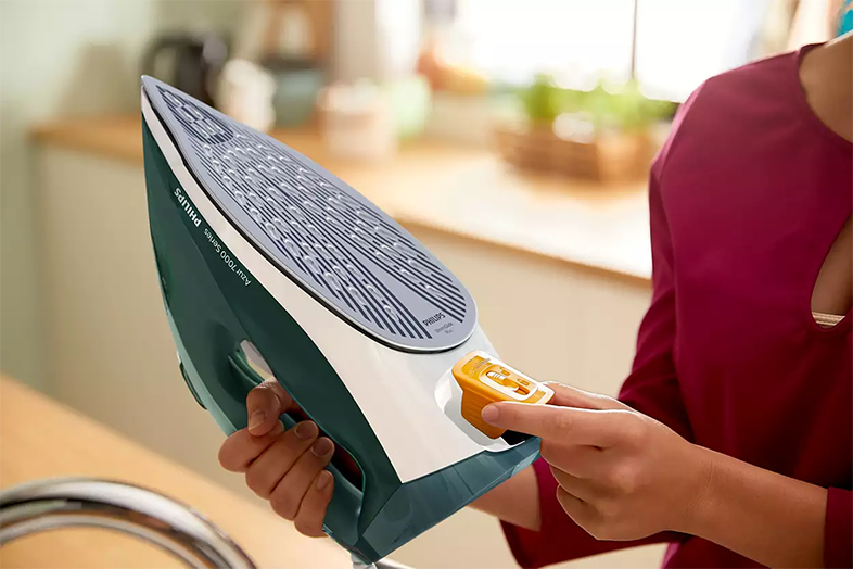 Egy személy kezei egy zöld Philips vasalót tartanak, egy sárga beállító tárcsát állítva.