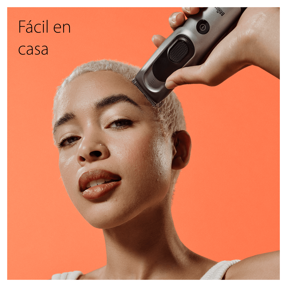 Mujer se afeita la cabeza con una recortadora sobre un fondo naranja. Texto: 'Fácil en casa'.