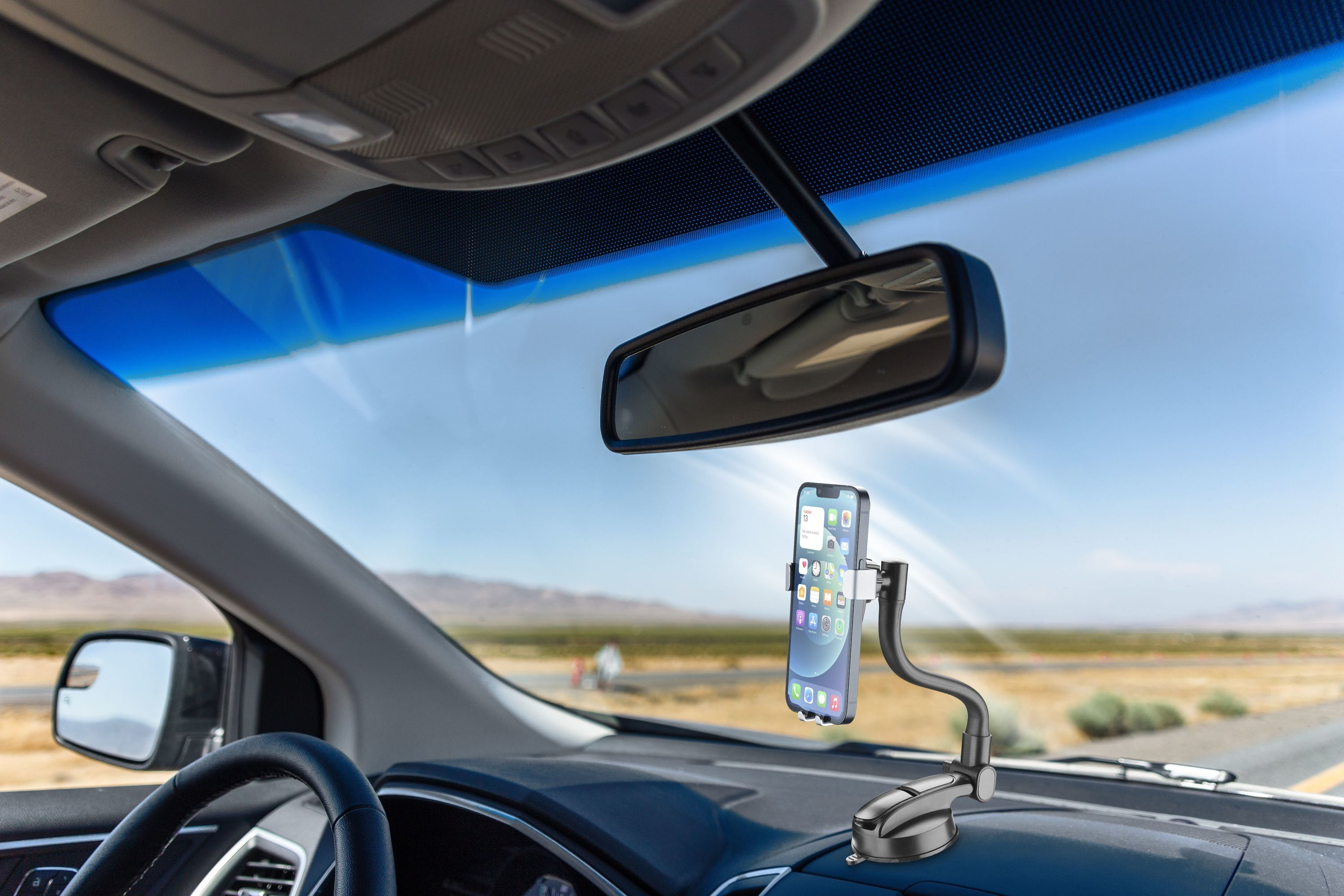 Toma interior de un coche. Un smartphone en un soporte en el salpicadero, con la carretera y el cielo visibles.