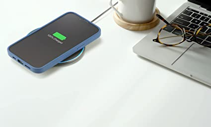 Un teléfono se carga de forma inalámbrica en una almohadilla, mostrando '100% Cargado' junto a una laptop.