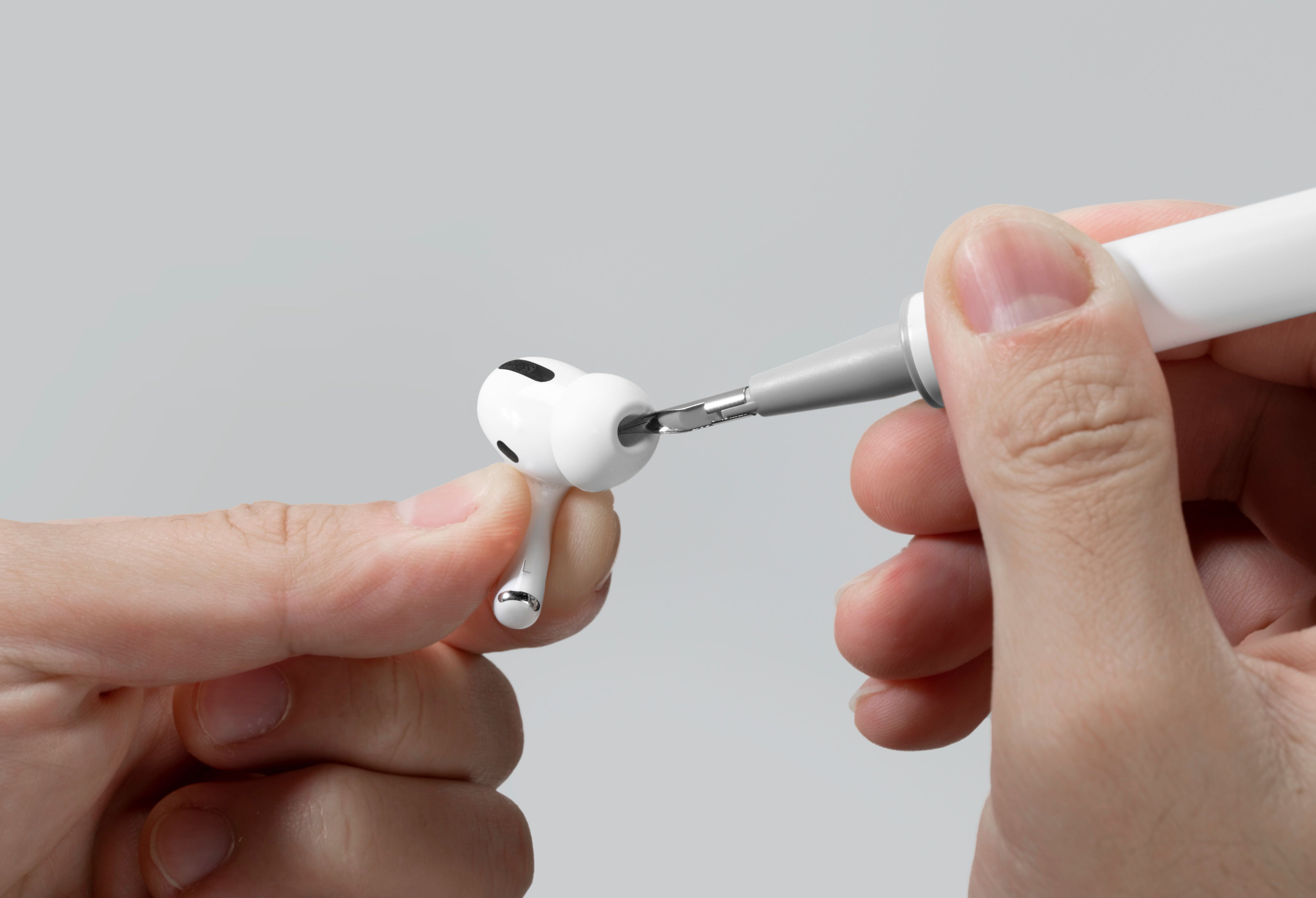 Une personne utilise un outil de nettoyage sur un AirPod blanc. Mise au point sur l'AirPod et l'outil.