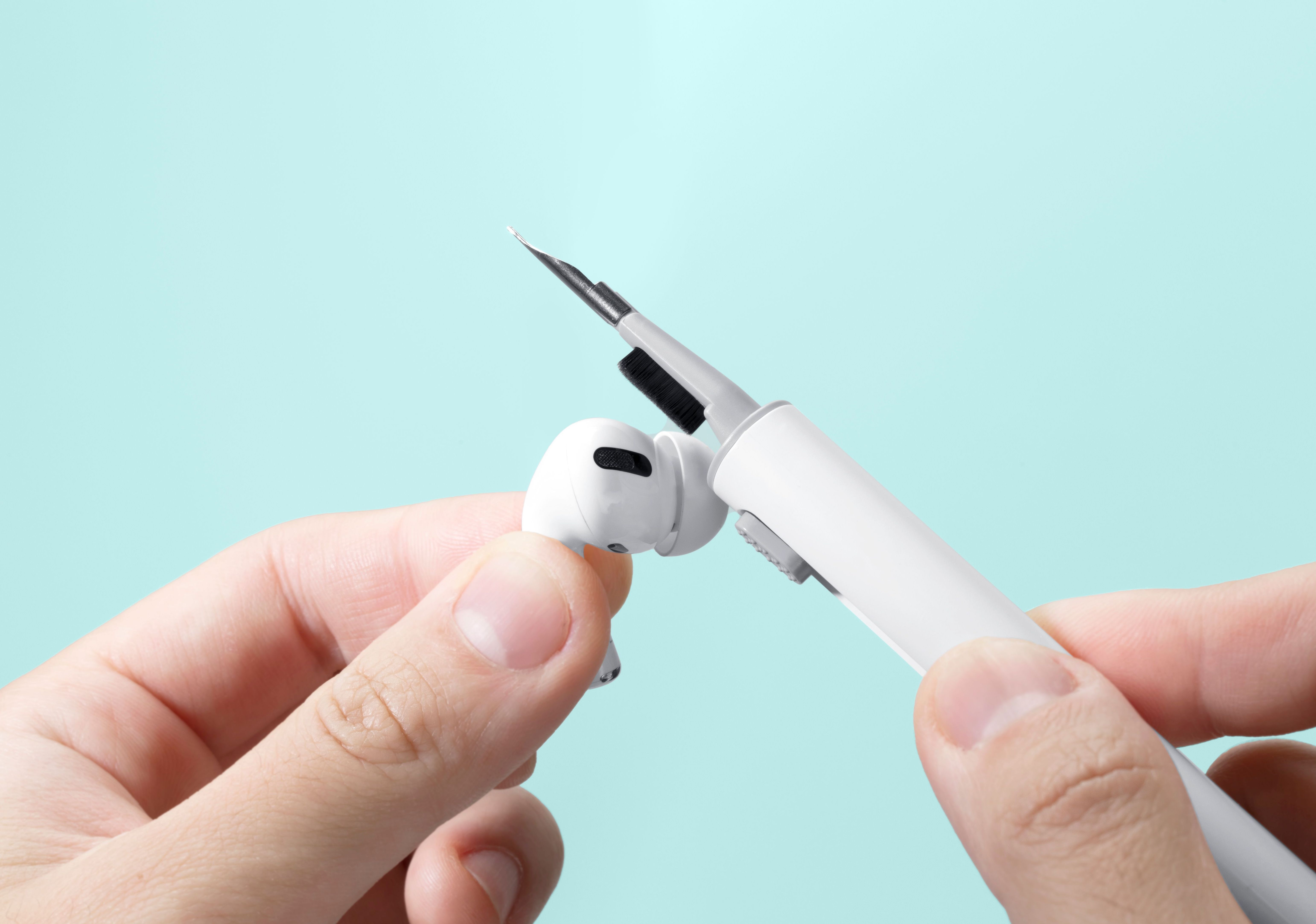 Mains nettoyant un écouteur blanc avec un outil de nettoyage.