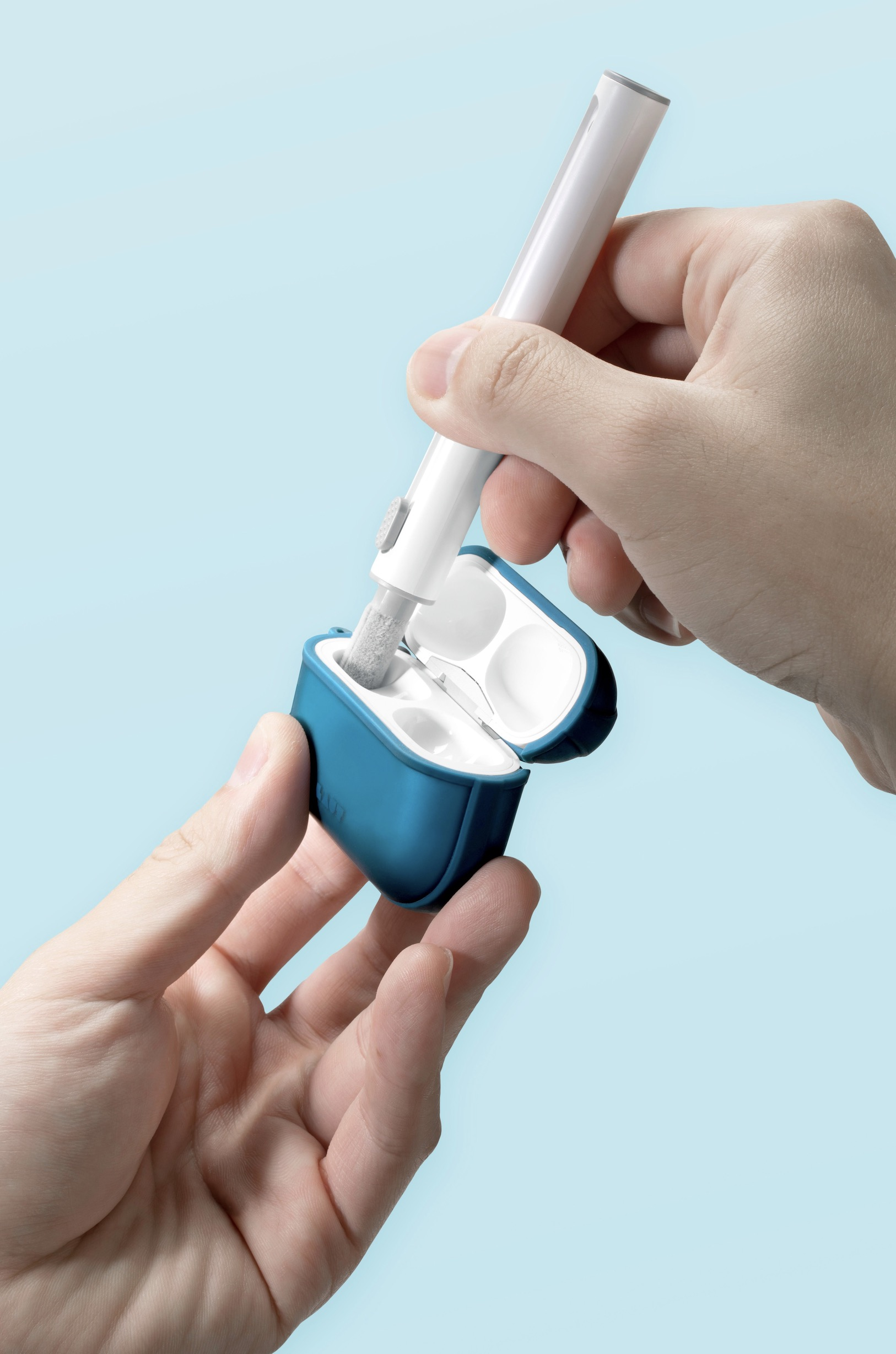 Une main nettoyant un étui d'écouteurs bleu avec un outil de nettoyage, sur fond bleu clair.
