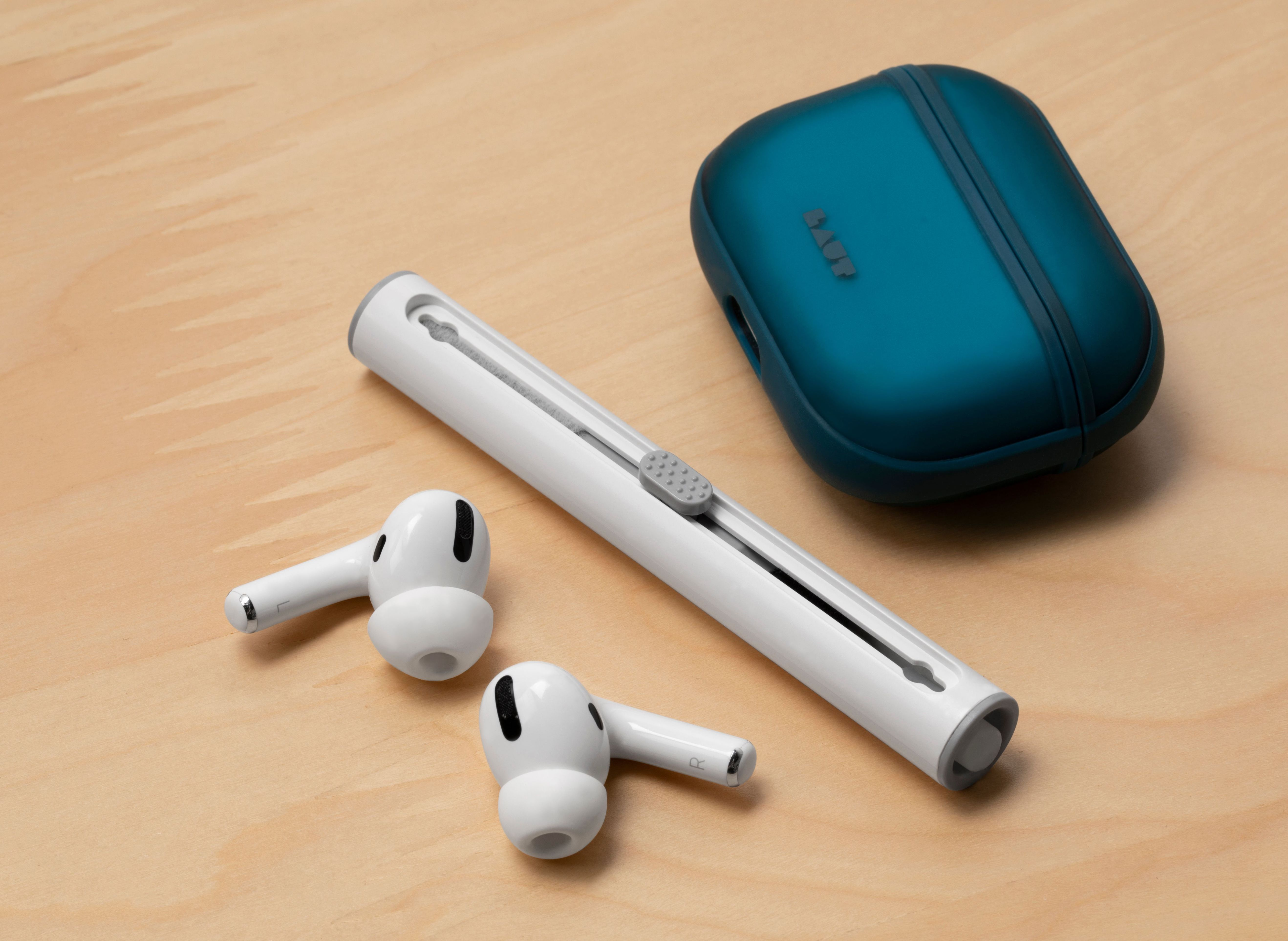 Écouteurs blancs et un outil de nettoyage à côté d'un étui bleu pour écouteurs sur une surface en bois.