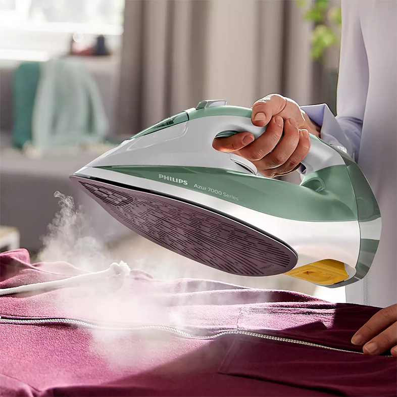 Személy bordó kapucnis pulóvert vasal egy zöld-fehér Philips Azur 7000 Series vasalóval. Gőz száll fel.