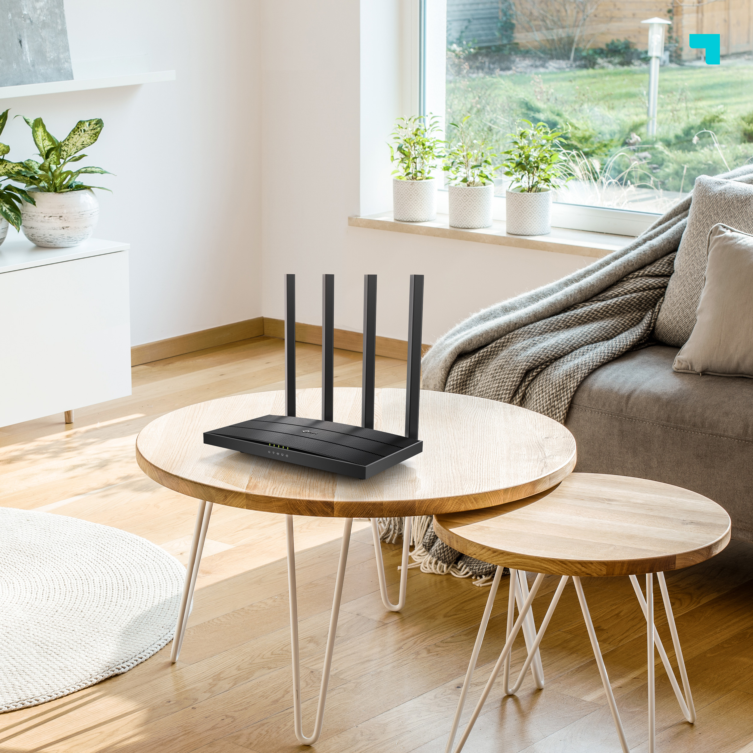 Router negro en una mesa. 4 antenas. Dos mesas de madera y un sofá en el fondo.