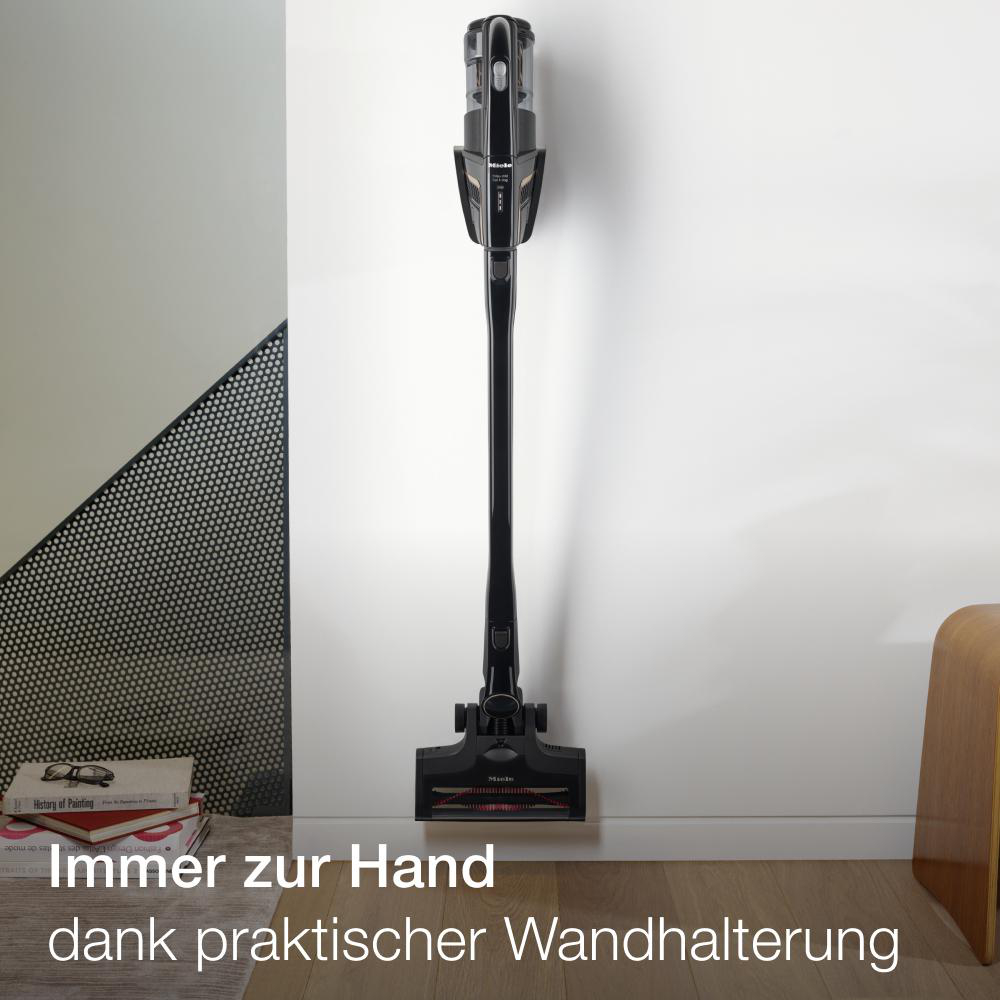 Schwarzer Akku-Staubsauger hängt an einer Wand, mit Text über Wandhalterung und Praktikabilität.