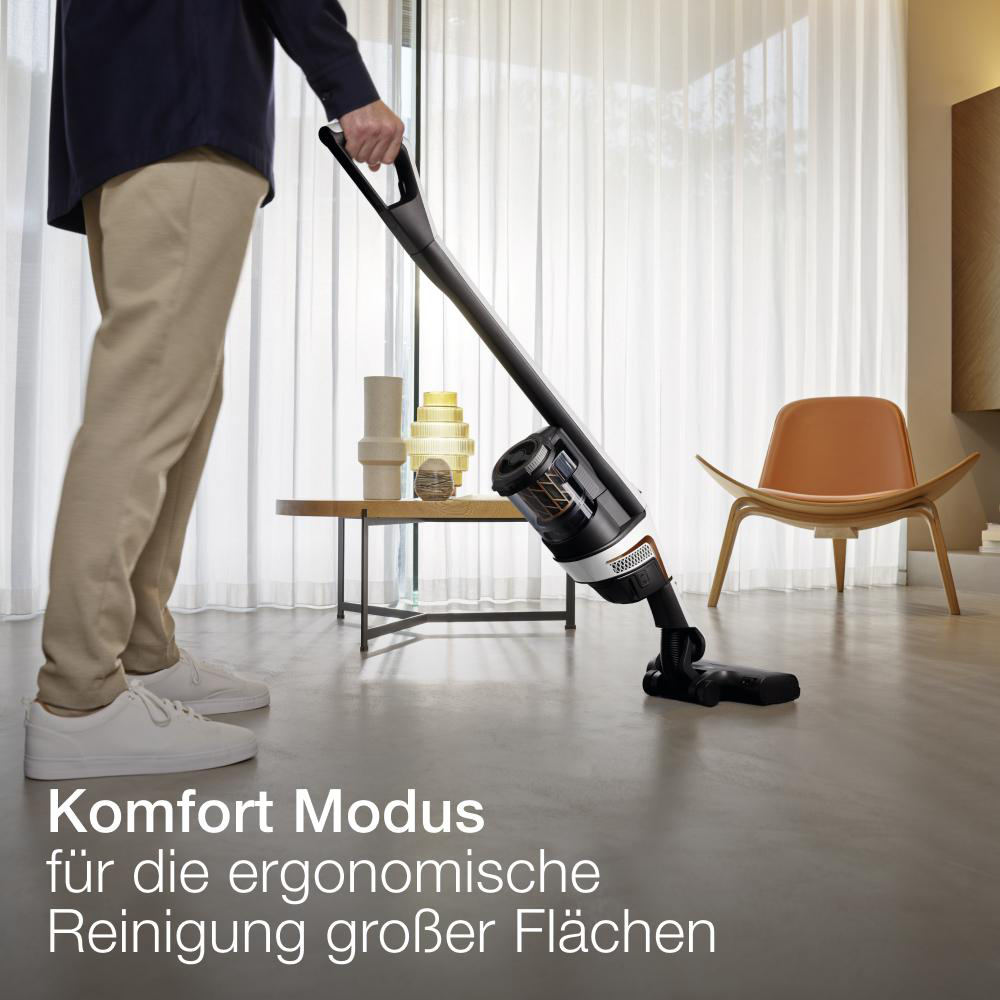 Eine Person, die mit einem schwarz-orangenen Staubsauger den Boden saugt.