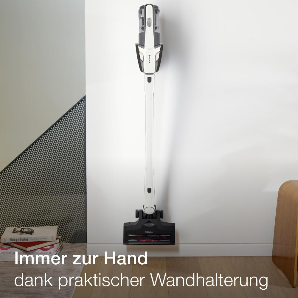 Ein weißer und schwarzer Staubsauger hängt an einer weißen Wand. Text: Immer zur Hand dank praktischer Wandhalterung.