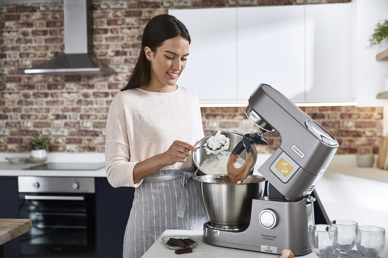 Eine Frau fügt Sahne in eine silberne Küchenmaschine in einer Küche hinzu.