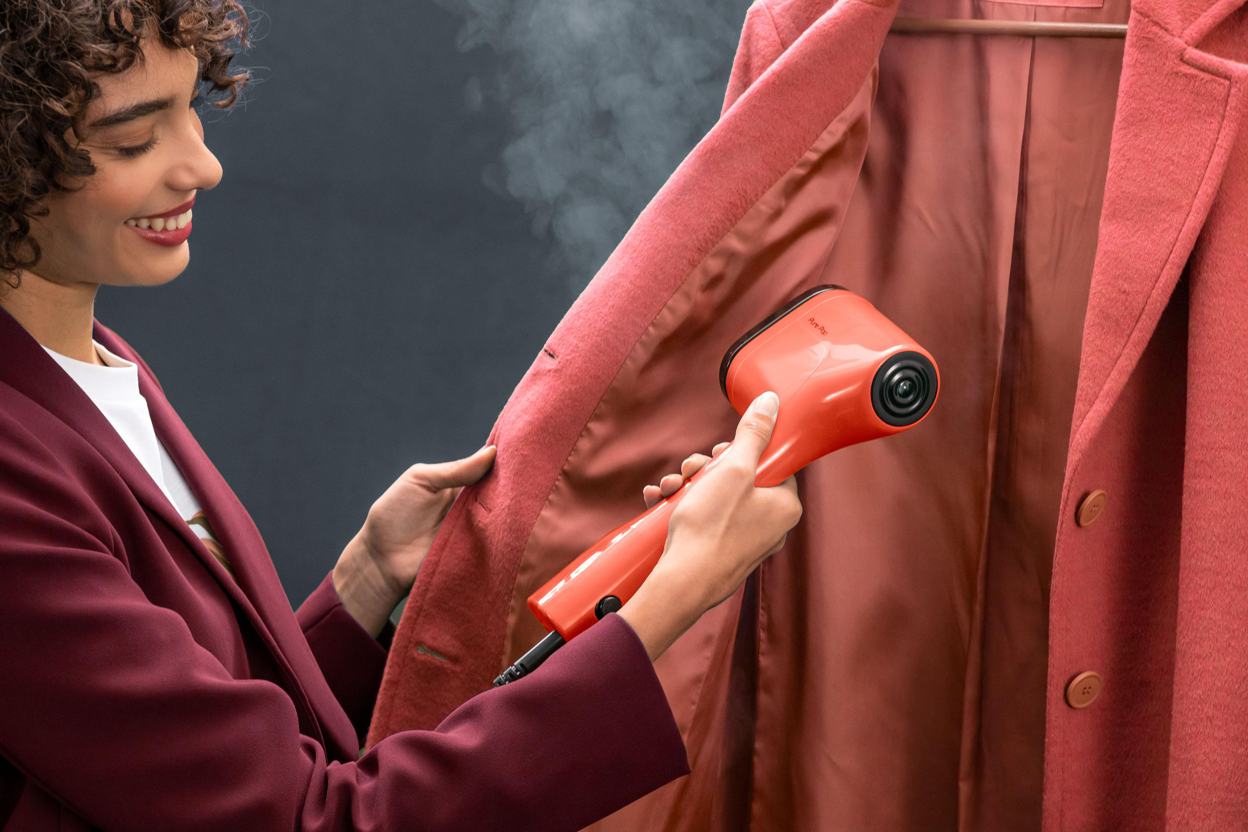 Eine Frau, die einen orangenen Steamer an einem rosa Mantel verwendet.