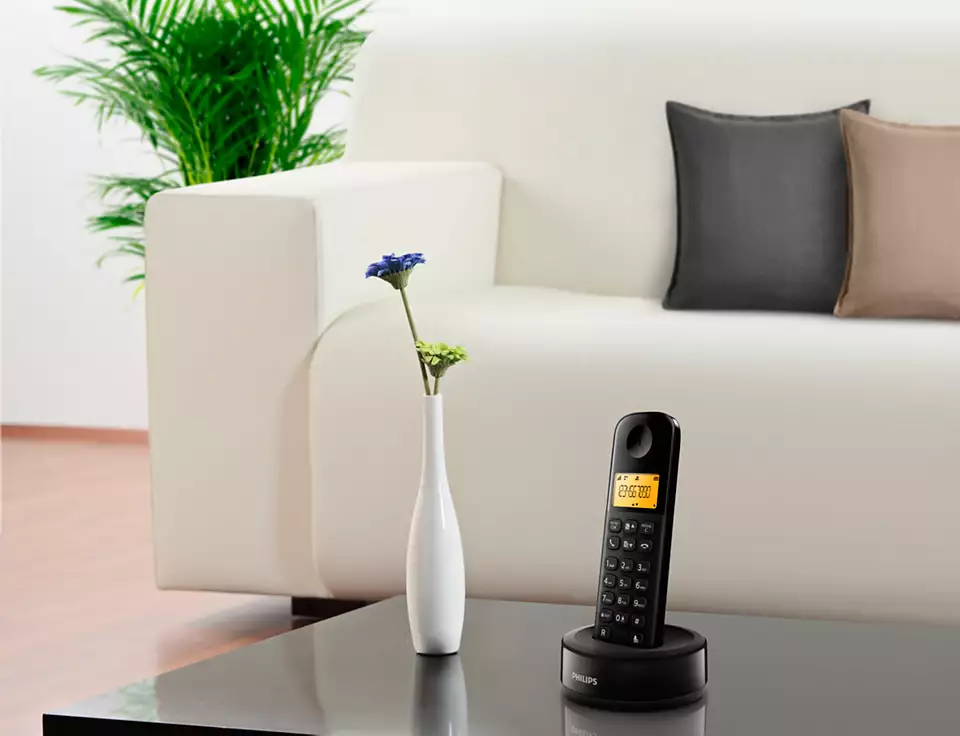 Téléphone sans fil sur table avec vase et canapé en arrière-plan.