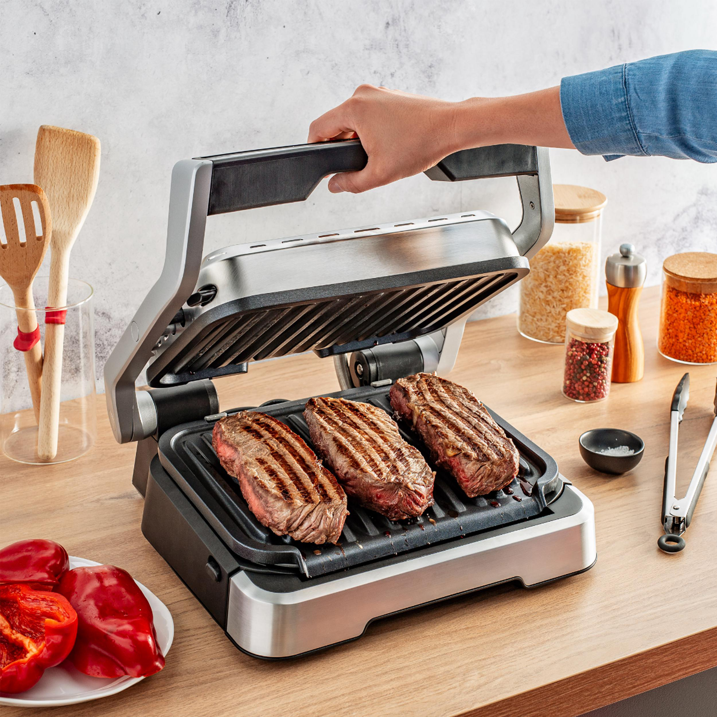 Steaks auf einem Grill, Hand hält Grilldeckel, mit Küchenartikeln.