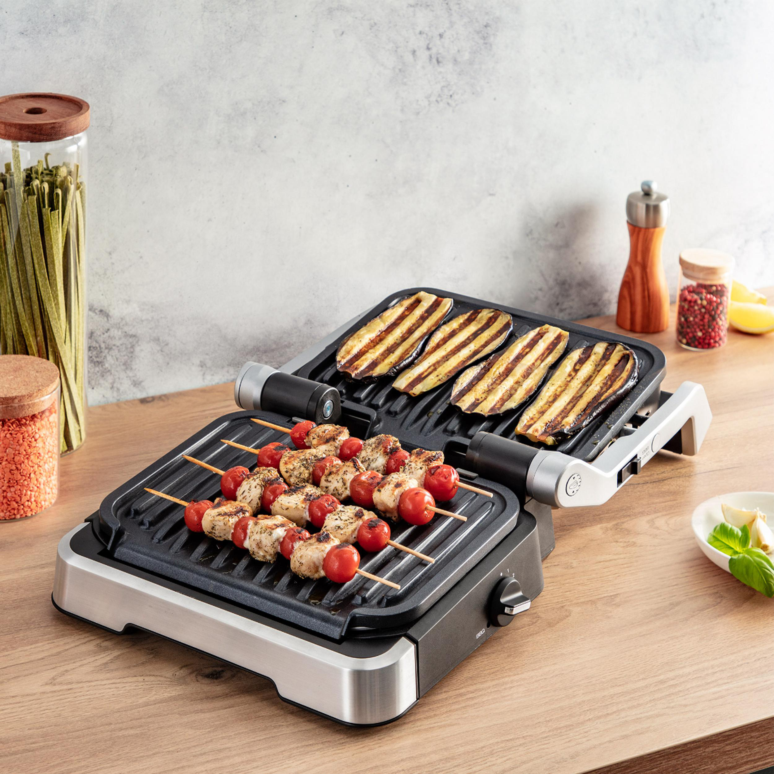 Grill mit Spießen und gegrilltem Gemüse auf Holzoberfläche.