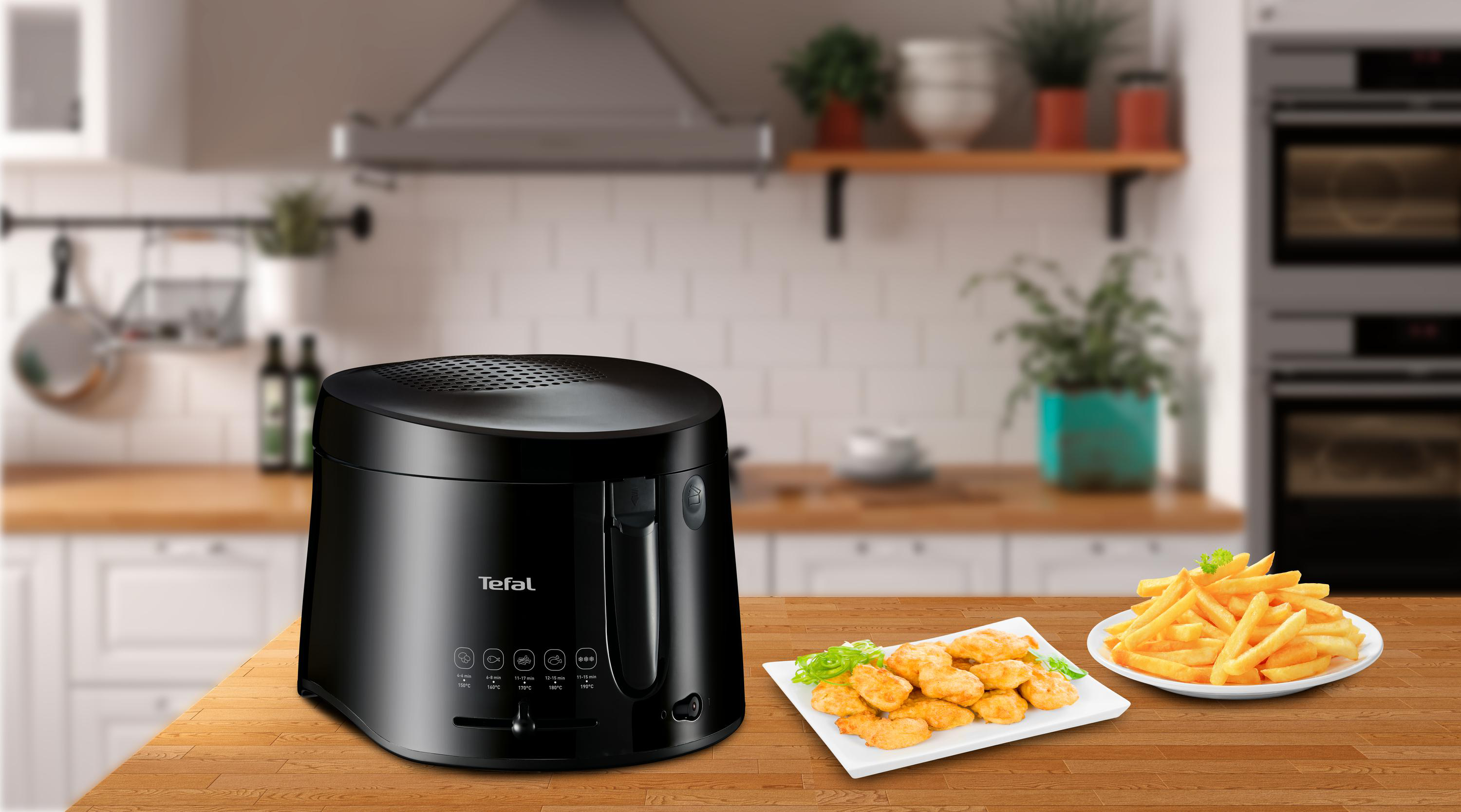 Schwarze Tefal Fritteuse mit Pommes und Chicken Nuggets auf Holzoberfläche.