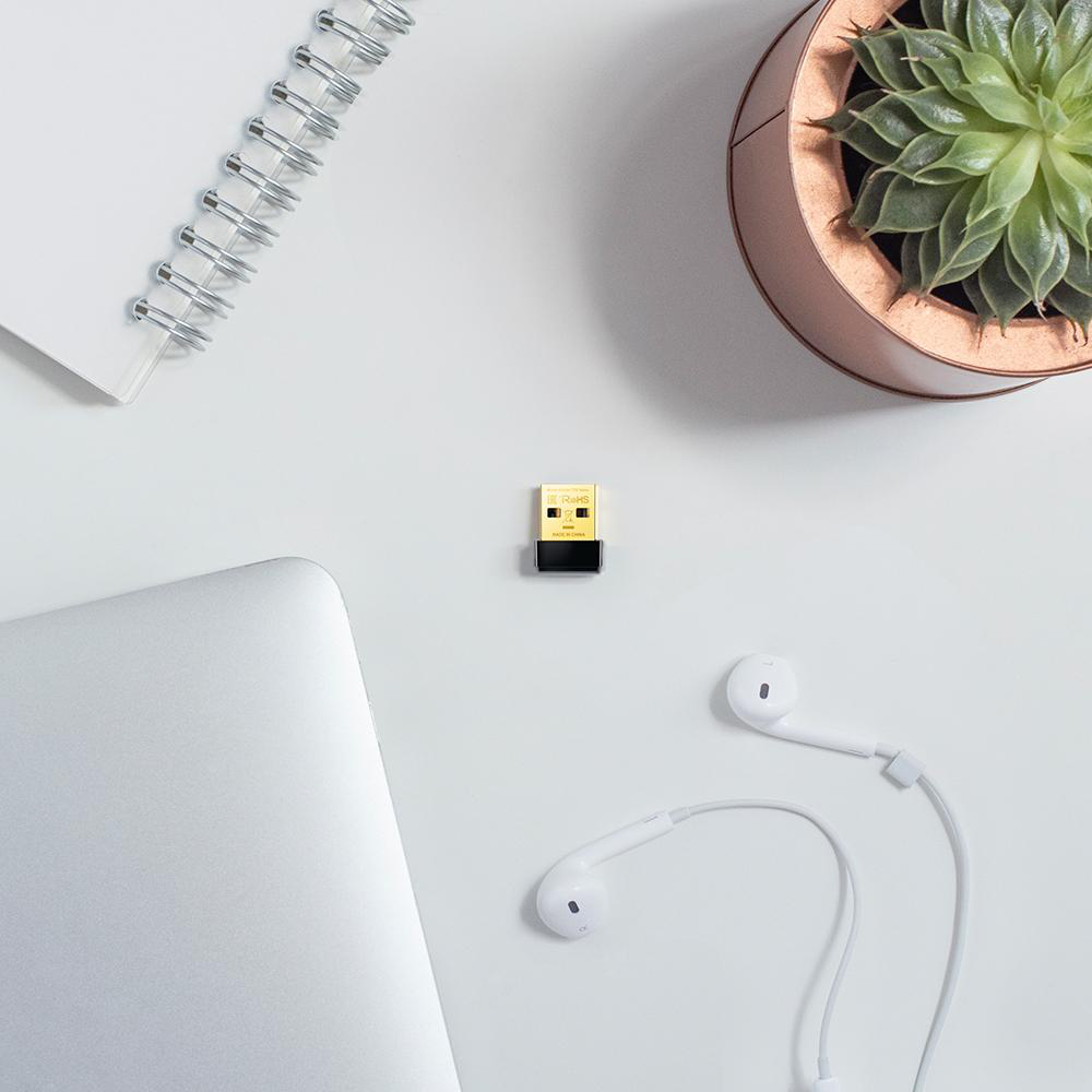 Ein Schreibtisch mit Laptop, USB-Dongle, Ohrhörern, Notizbuch und kleiner Pflanze.
