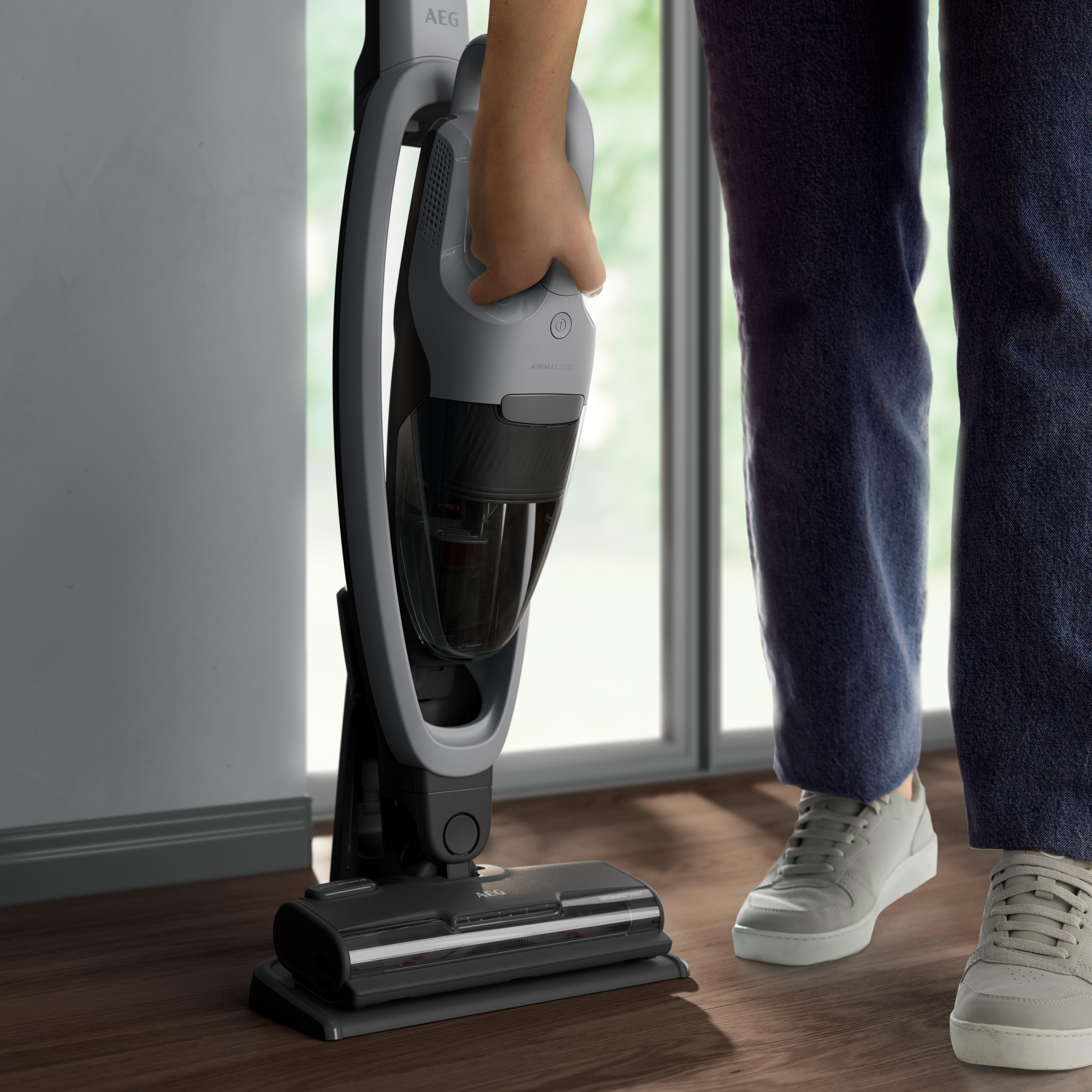 Eine Person, die einen grau-schwarzen AEG-Staubsauger auf einem Holzboden verwendet.
