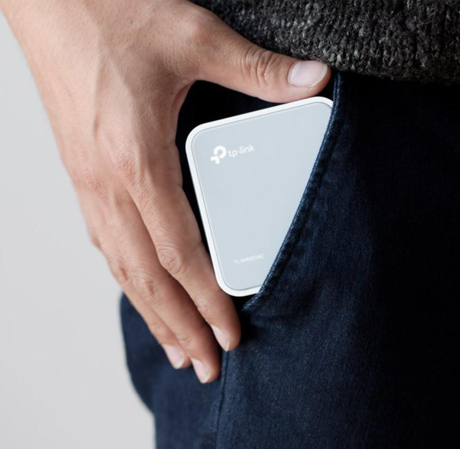 Die Hand einer Person hält einen kleinen, grauen TP-Link-Router in einer dunkelblauen Jeans-Tasche.