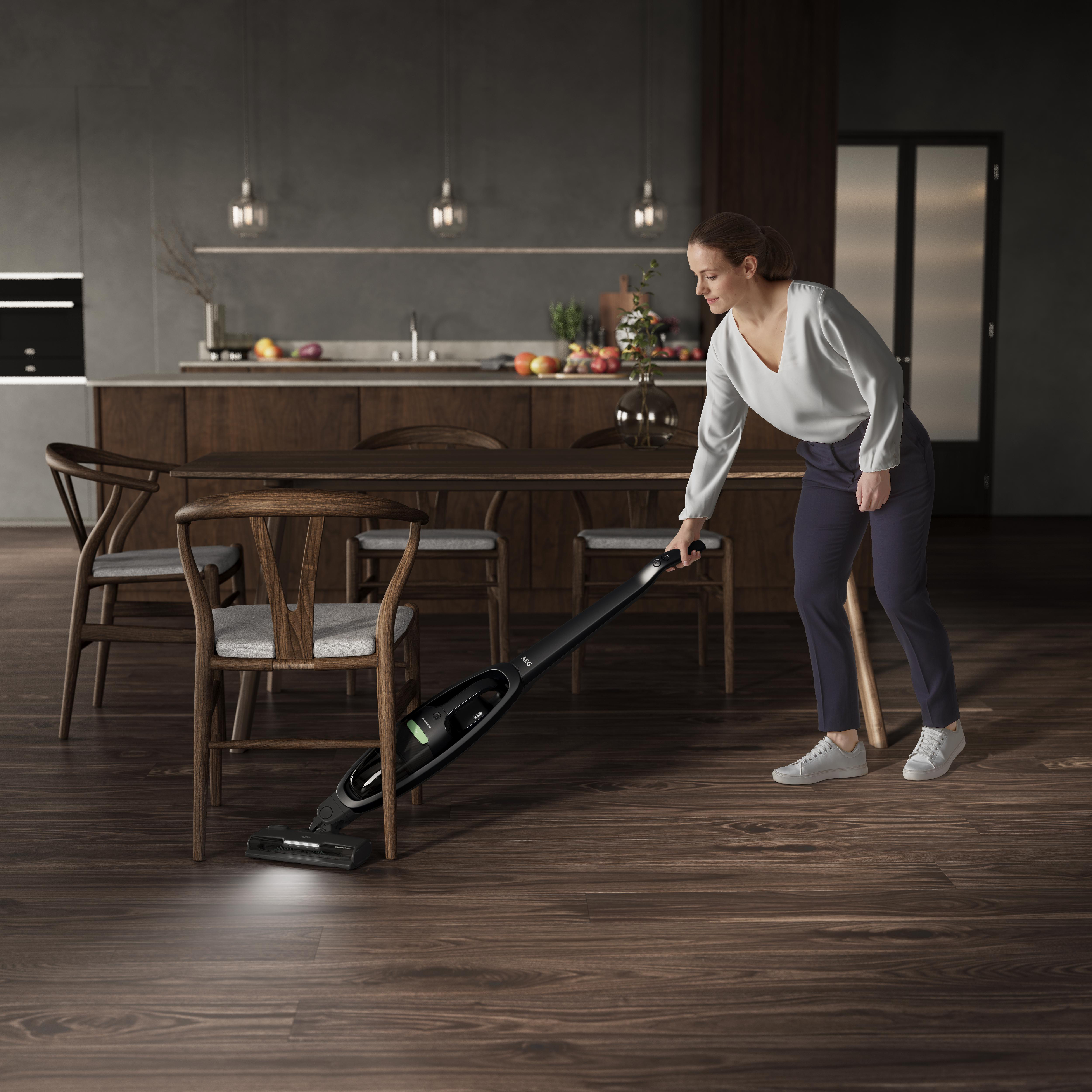 Eine Frau, die einen Holzboden in einer modernen Küche saugt, mit eingeschaltetem Licht.