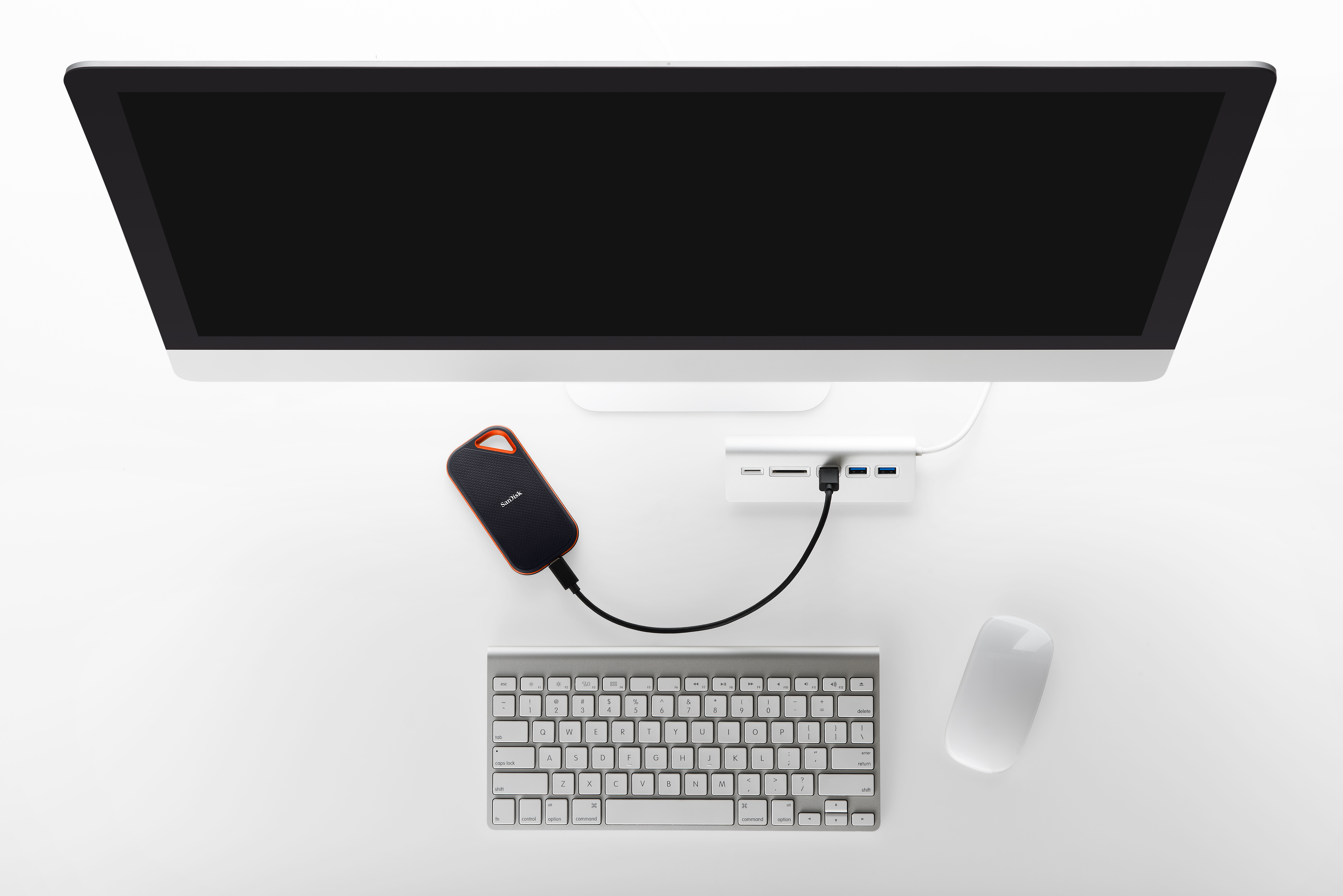 Beyaz yüzeyde monitör, klavye, fare, harici sabit disk ve hub'ın yukarıdan görünümü.