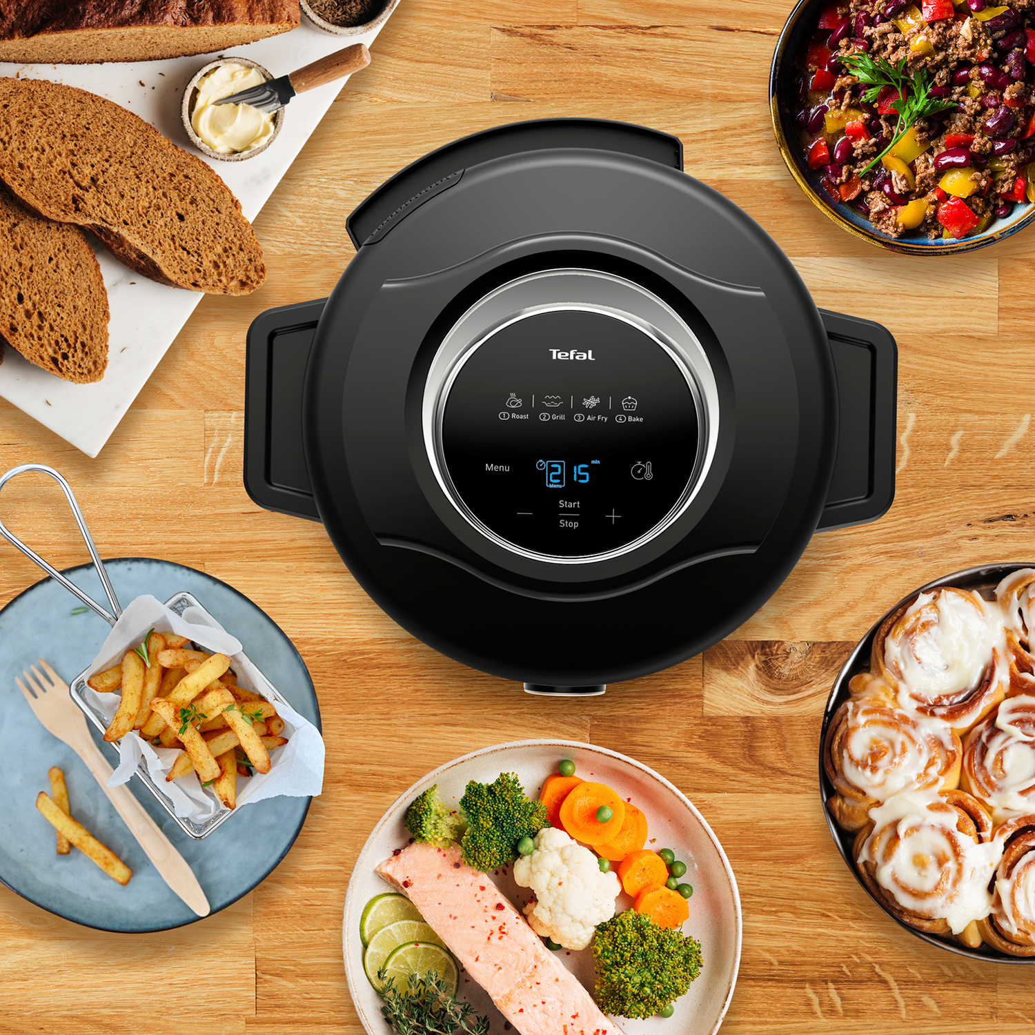 Zwarte airfryer met digitaal display, omringd door diverse gekookte gerechten op houten tafel.