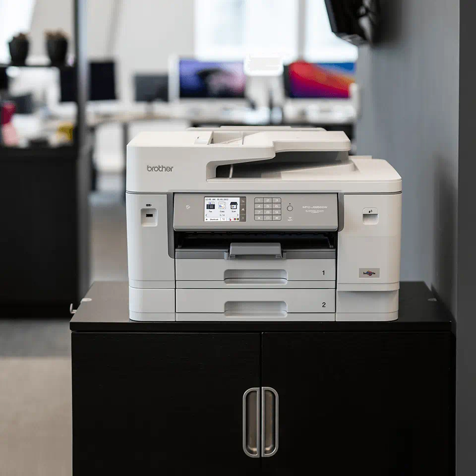 Une imprimante blanche sur une armoire noire dans un cadre de bureau, vue légèrement inclinée.