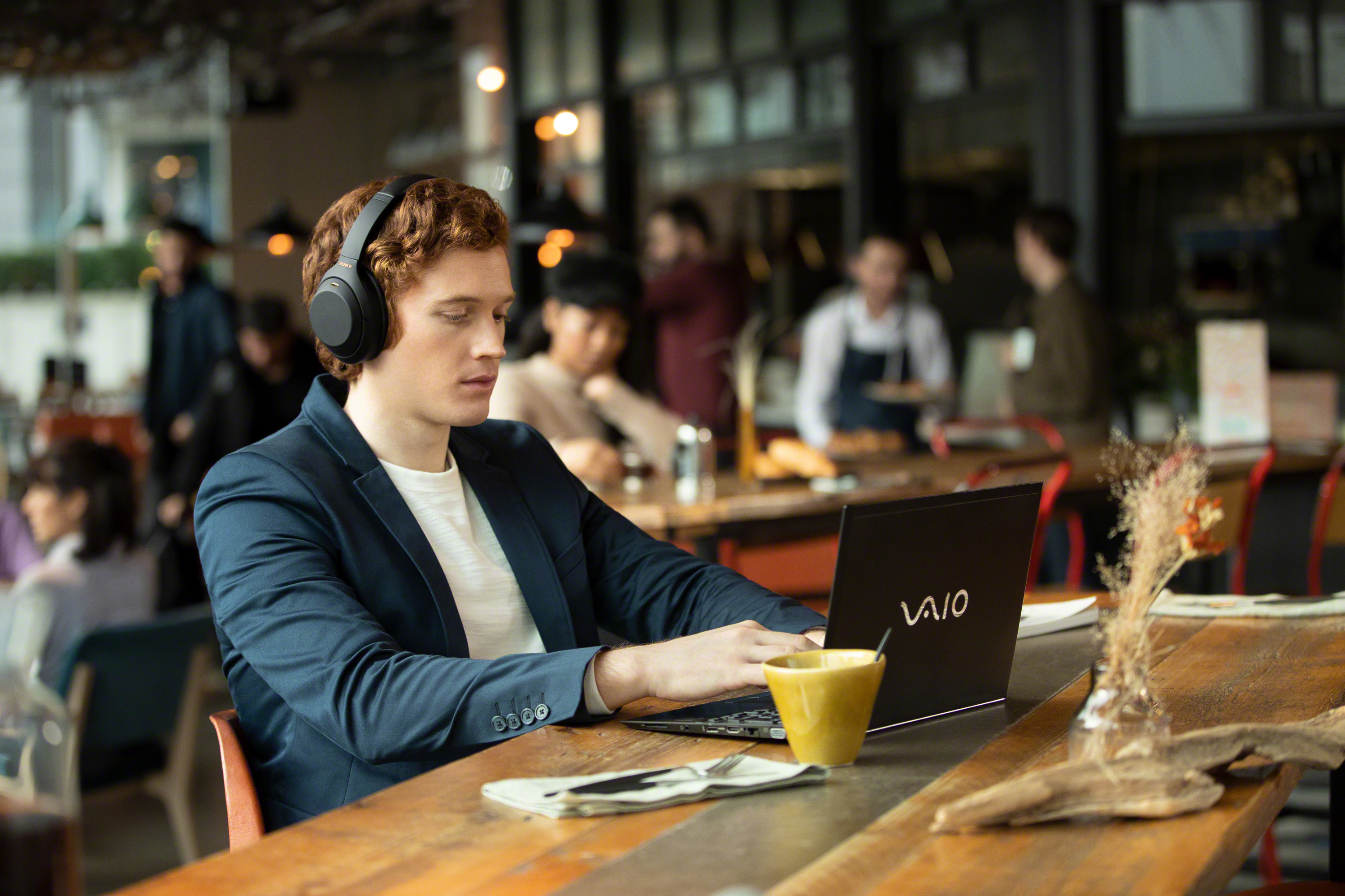 Mann mit Kopfhörern benutzt Laptop am Cafétisch, Kaffeetasse.