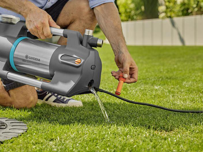 Mann schließt Gartenschlauch an Pumpe an, Wasser fließt.