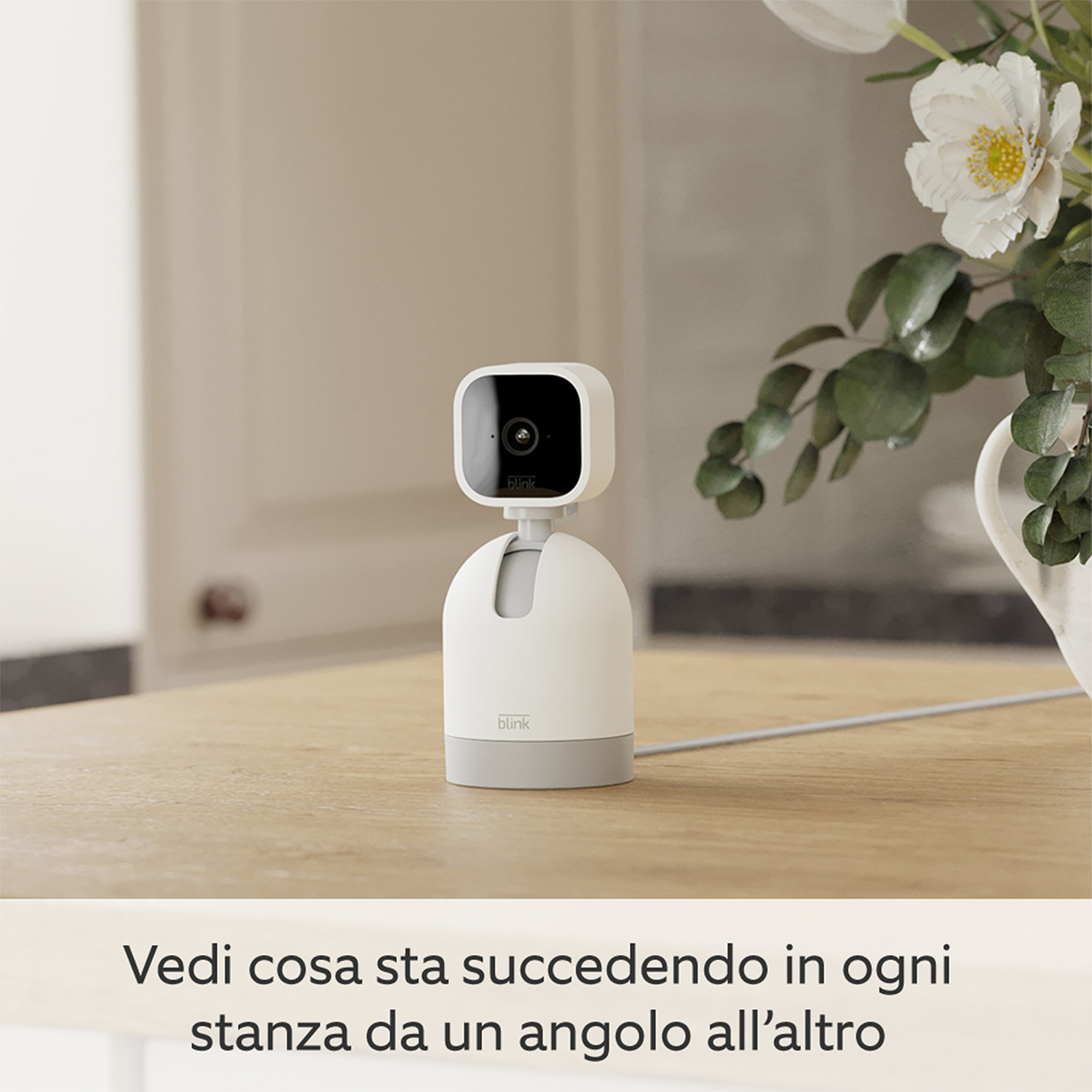 Una telecamera di sicurezza bianca e grigia su un tavolo di legno, in un ambiente domestico.
