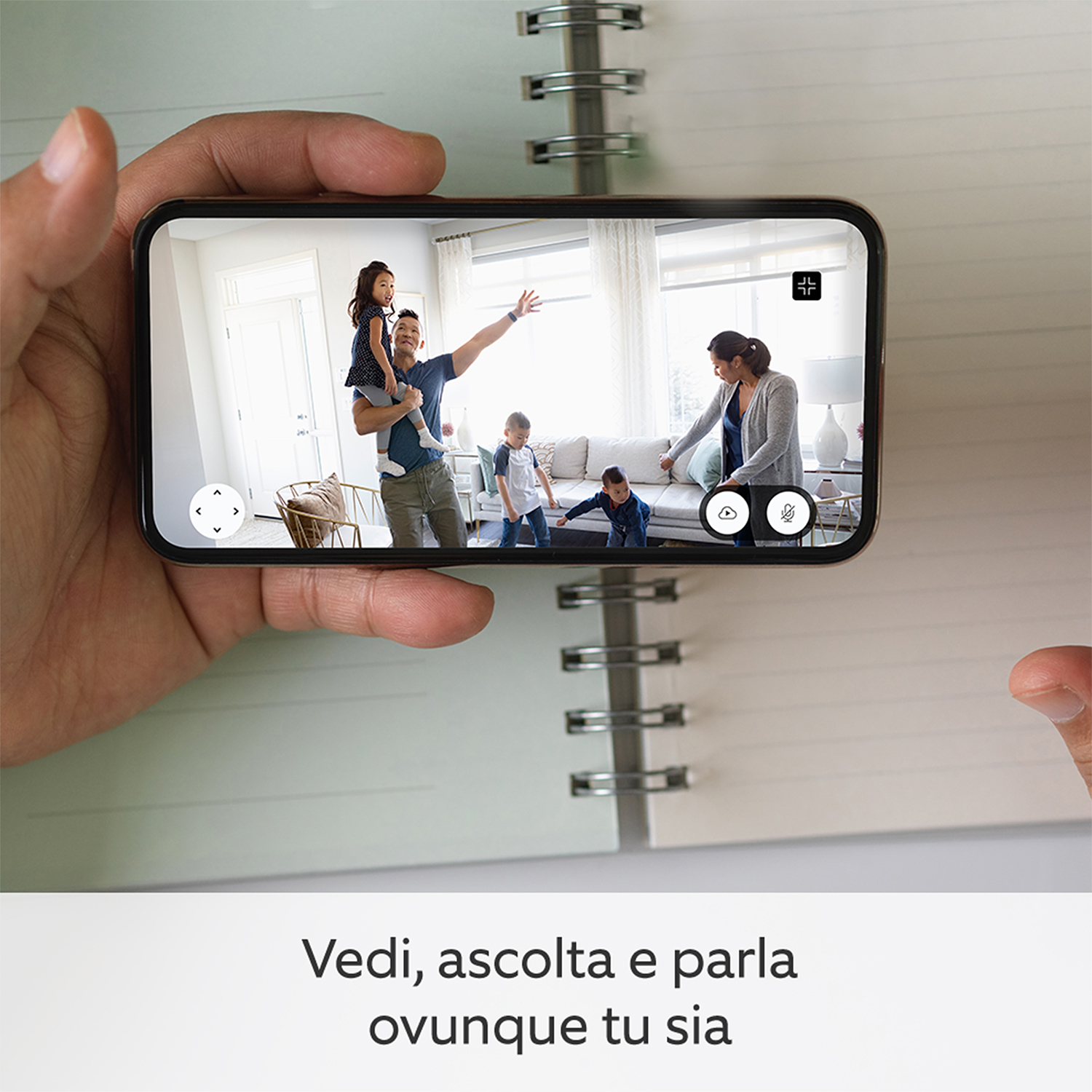 Un telefono tenuto in mano mostra una videochiamata con una famiglia in soggiorno. Il testo sottostante dice 'Vedi, ascolta e parla'.