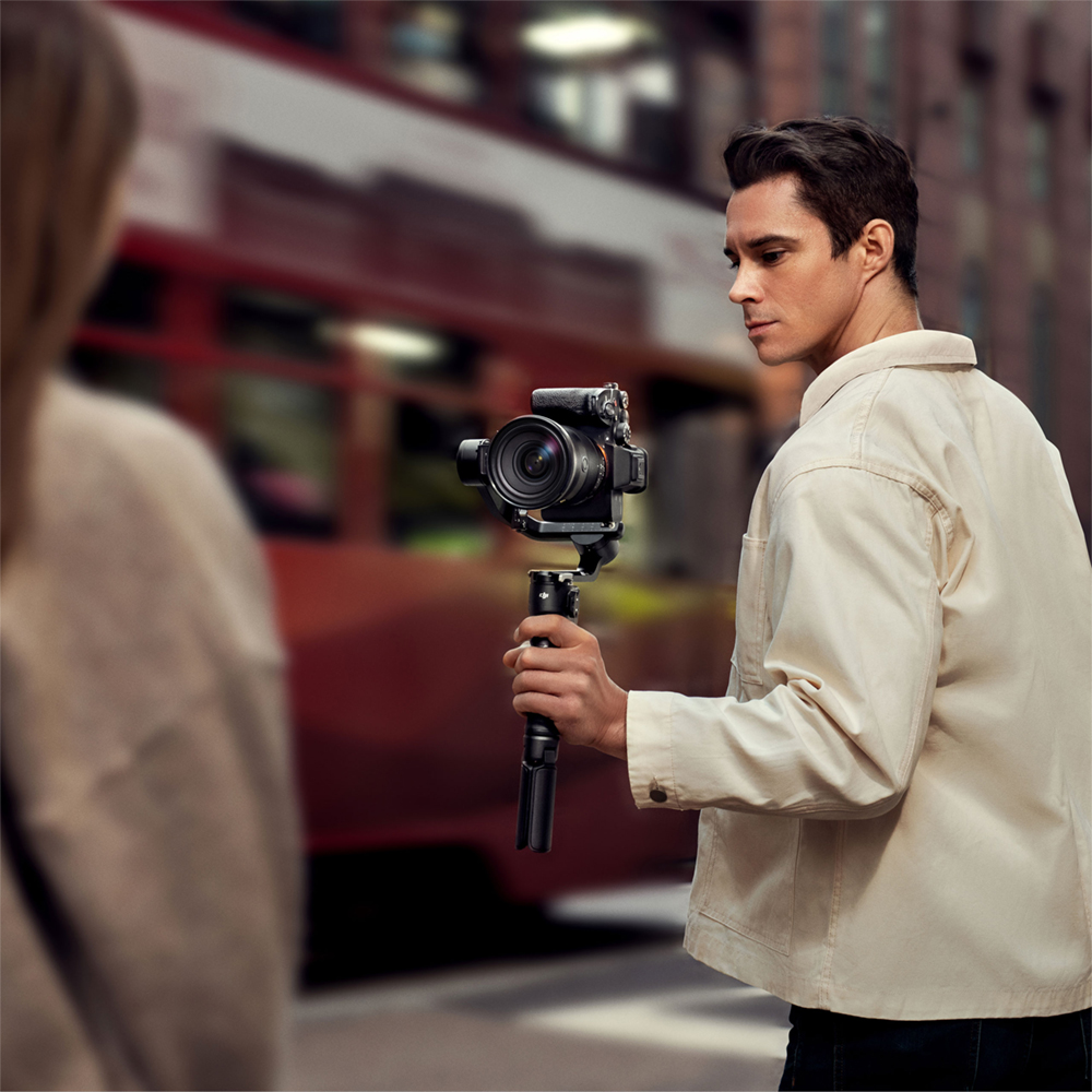 Un homme tenant une caméra sur un gimbal, avec un arrière-plan flou d'une rue de la ville.