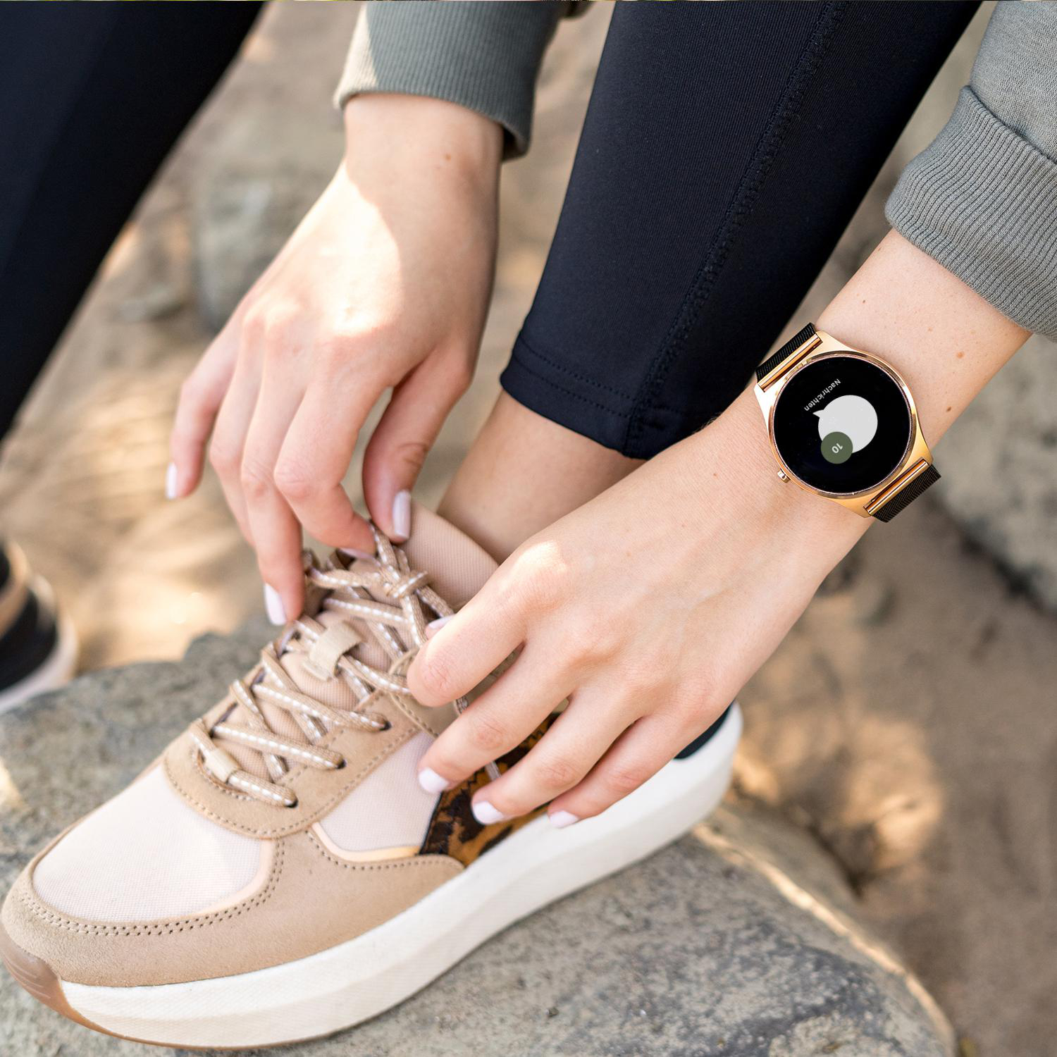 Hände einer Frau beim Schnüren eines Schuhs, eine Smartwatch am Handgelenk.