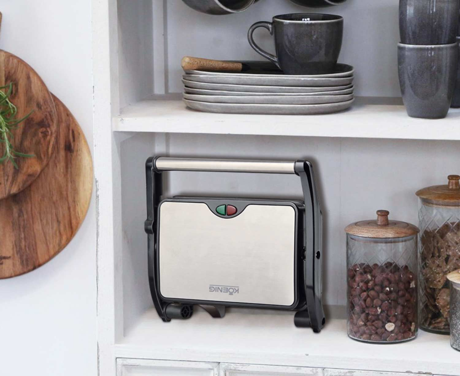 Macchina per sandwich su uno scaffale con taglieri in legno e barattoli sullo sfondo.