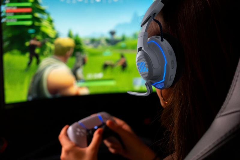 Person mit Gaming-Headset und Controller, spielt ein Spiel am Monitor.