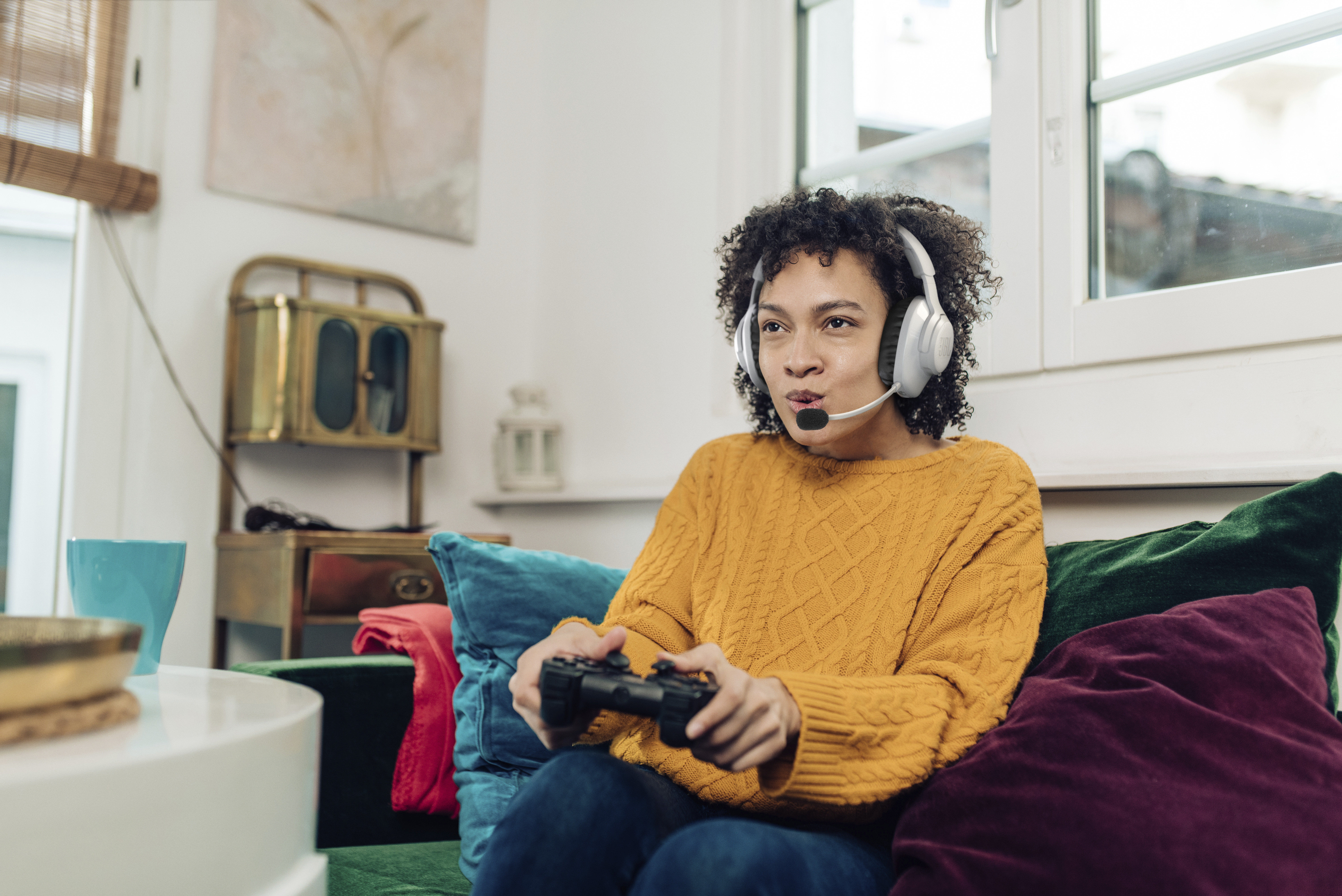 Frau spielt Videospiel, trägt Kopfhörer, hält Controller auf Sofa.