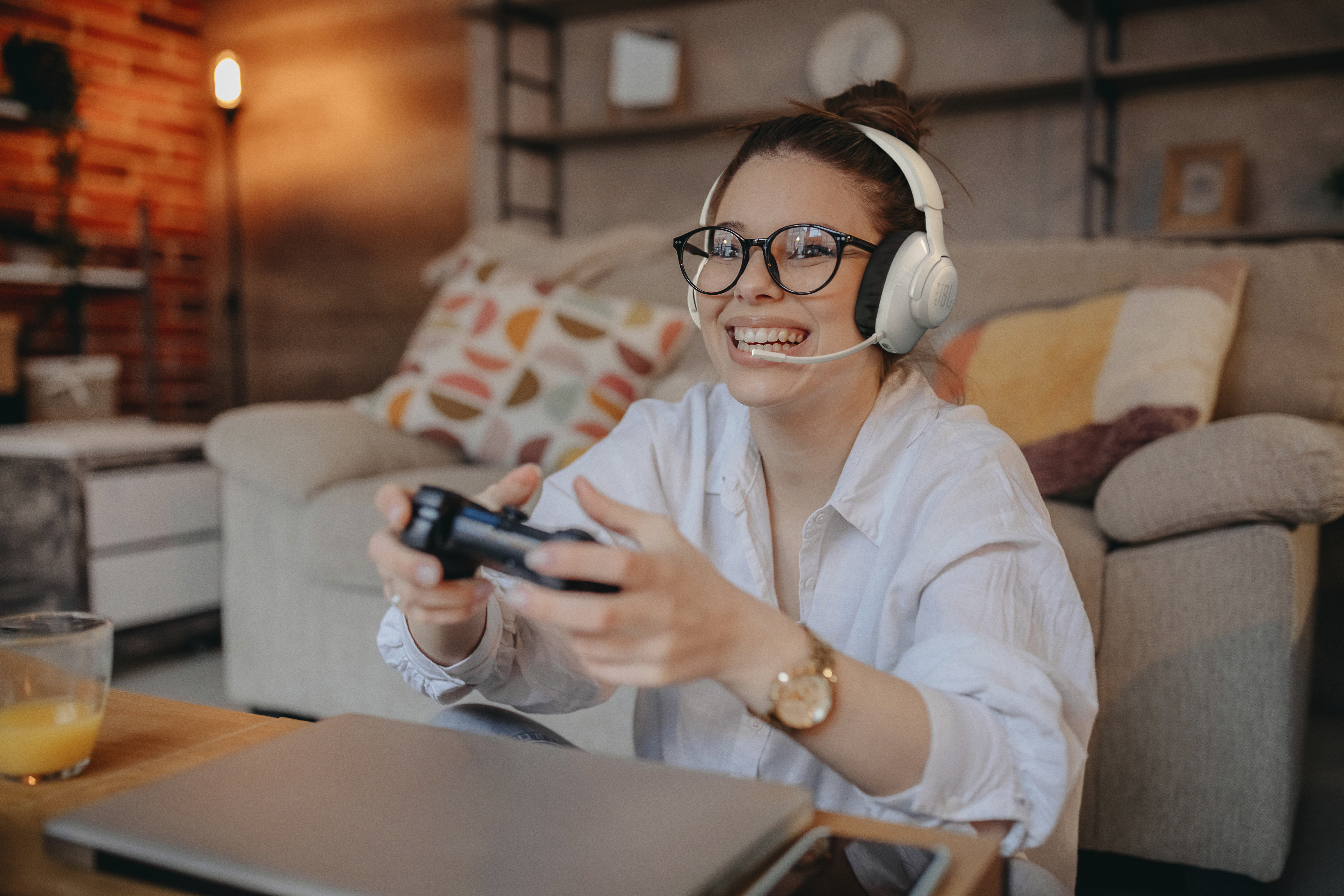 Eine Frau mit Headset und Brille lächelt, hält einen Controller und spielt ein Videospiel.