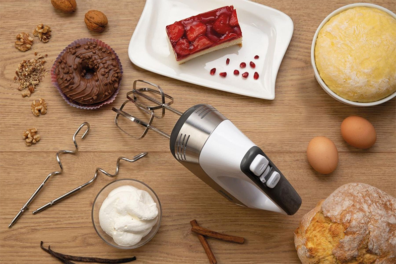 Fából készült asztal hozzávalókkal: mixer, fánk, sütemény, tészta, tojás, dió és fűszerek.