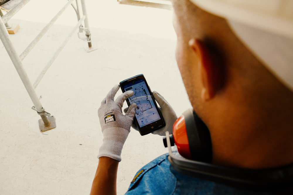 Une personne regardant un smartphone montrant un plan d'étage, sur un chantier.