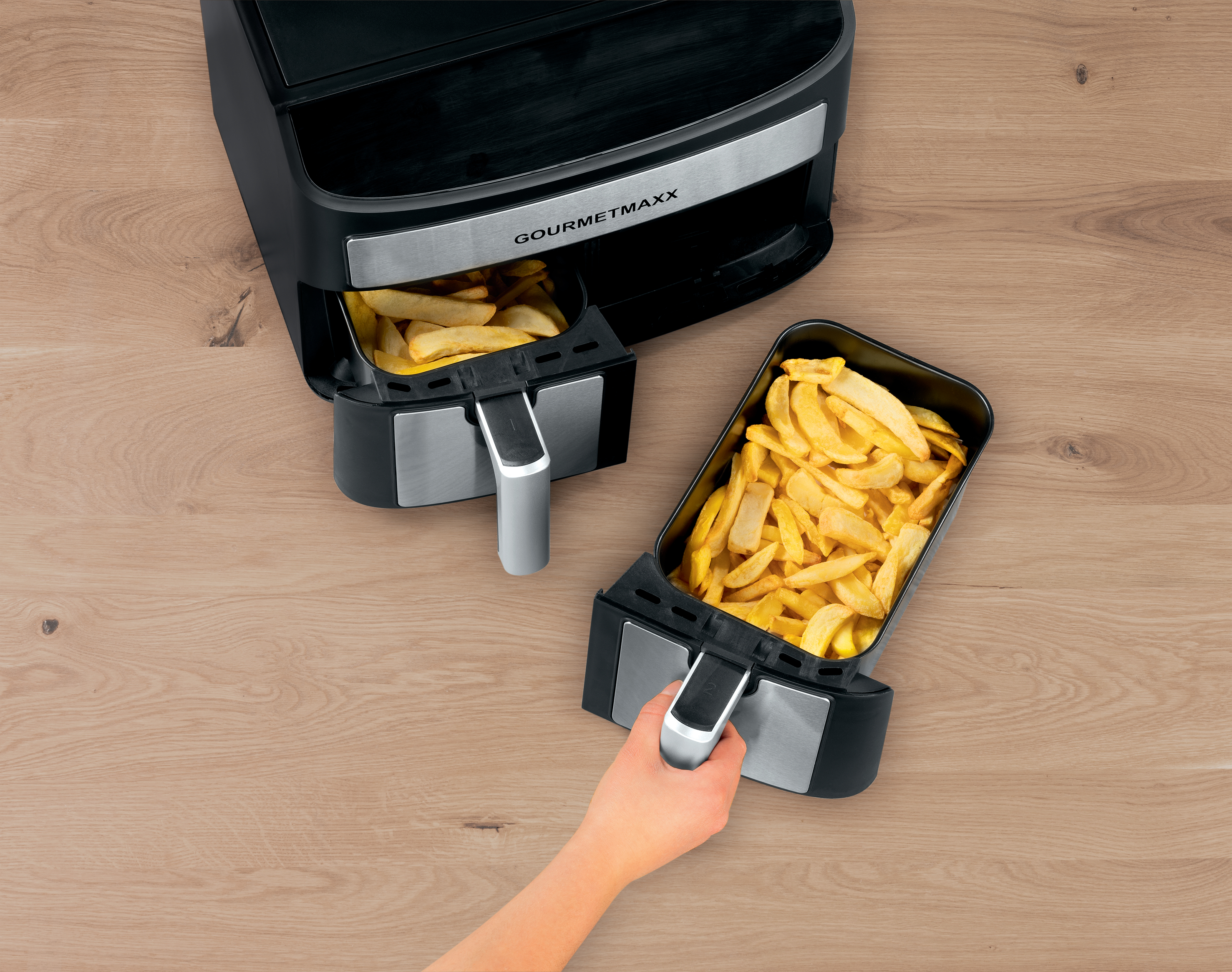 Heißluftfritteuse mit zwei Körben Pommes frites auf Holzoberfläche.