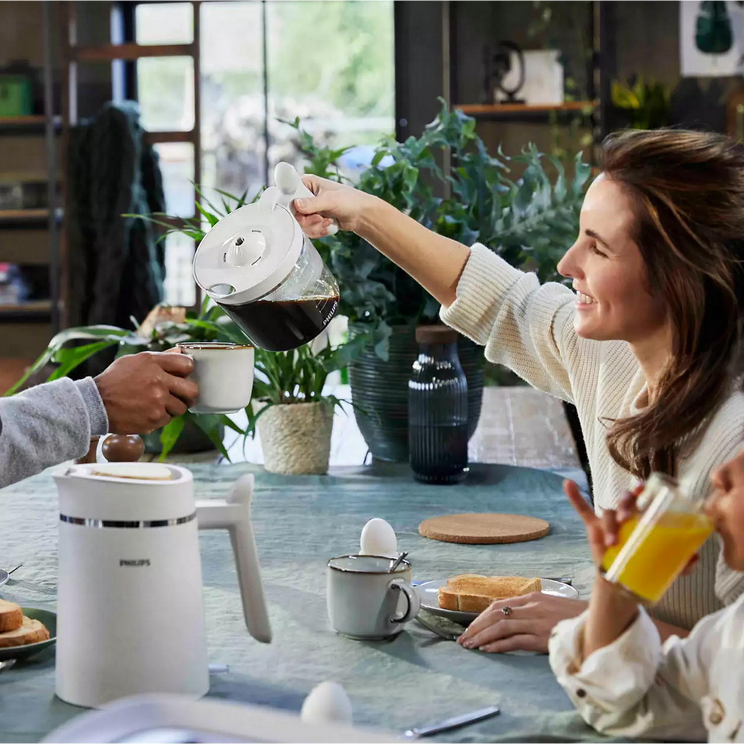 A woman pouring coffee from a carafe into a cup during a breakfast setting.
