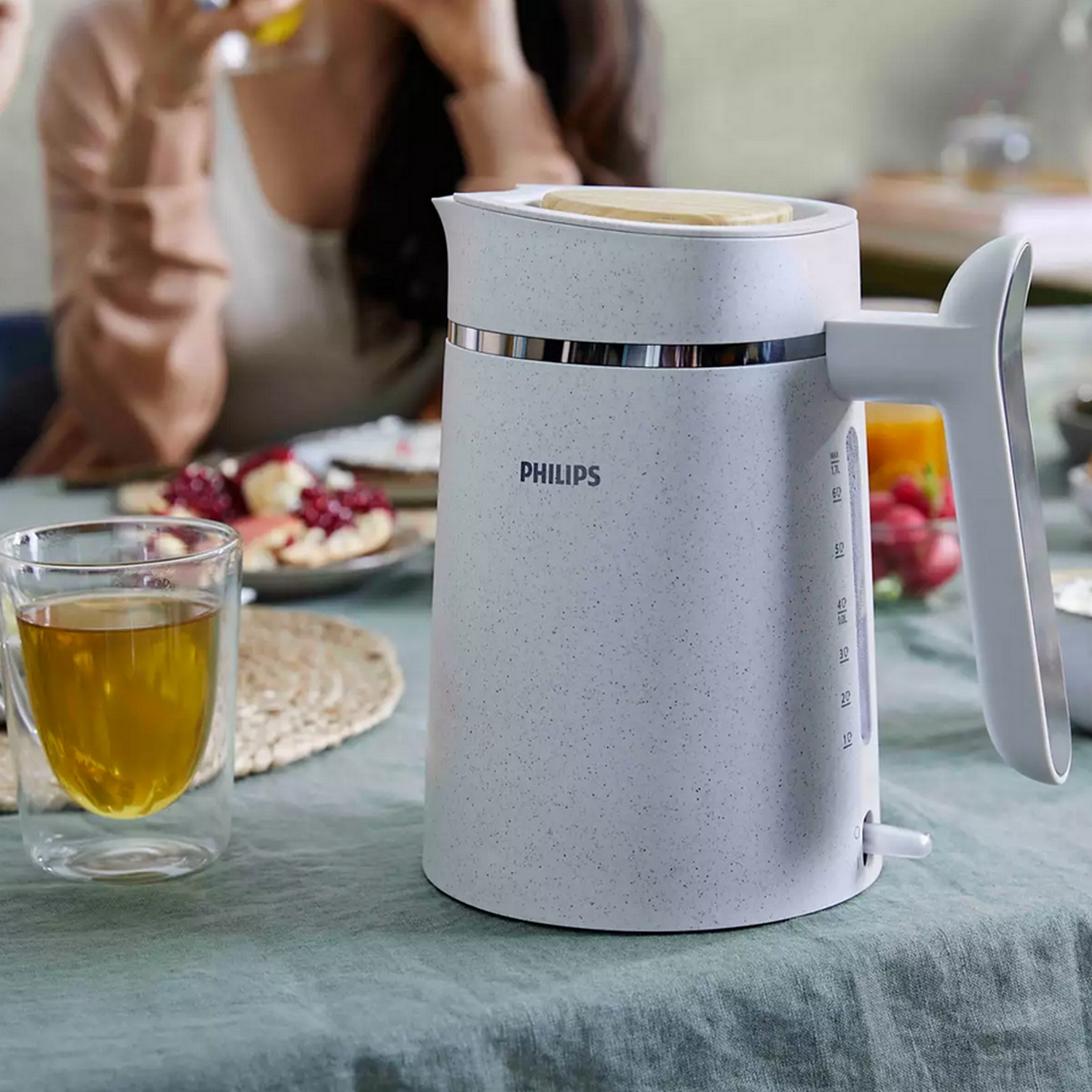 White Philips kettle with a glass of tea and food on a table. Table is covered with a cloth.