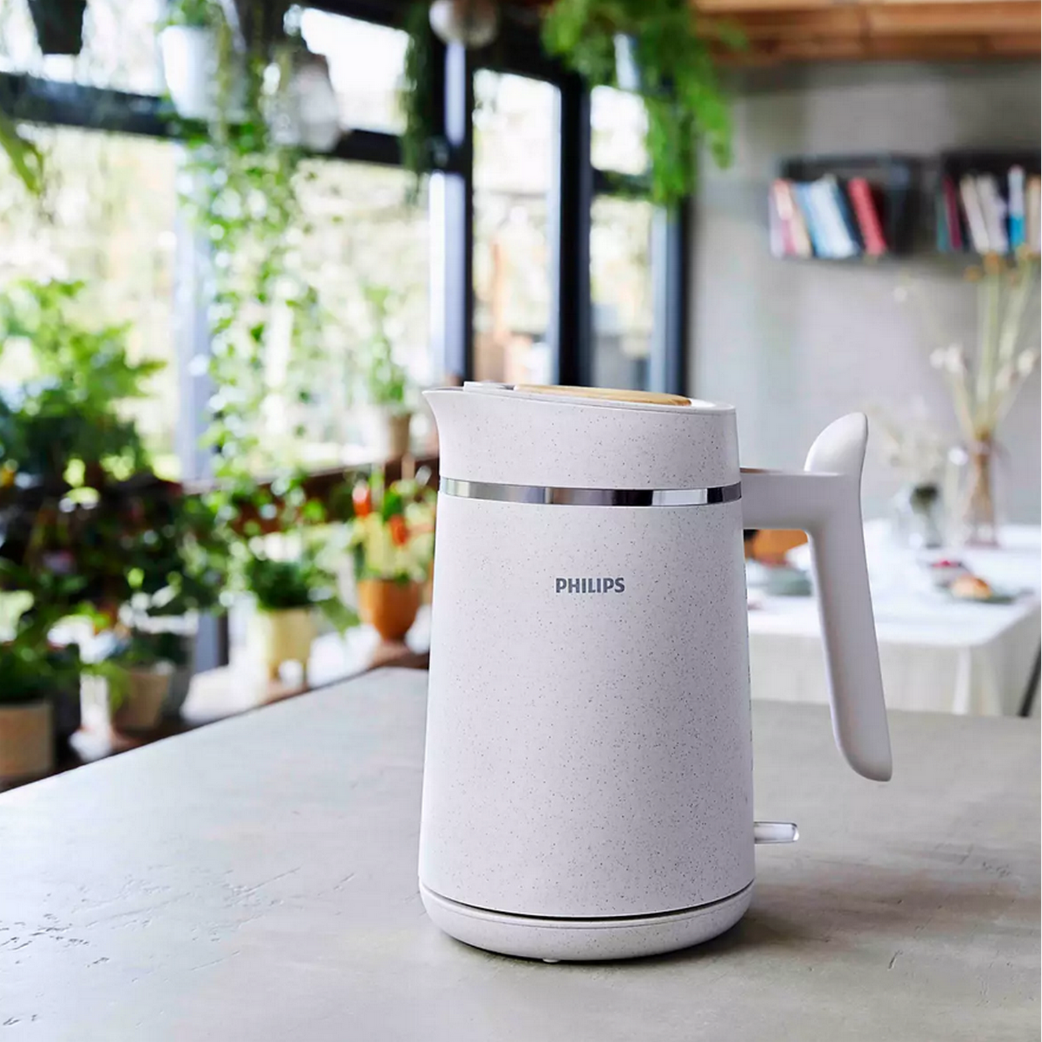 A white speckled Philips kettle on a counter, with a background of plants and windows.