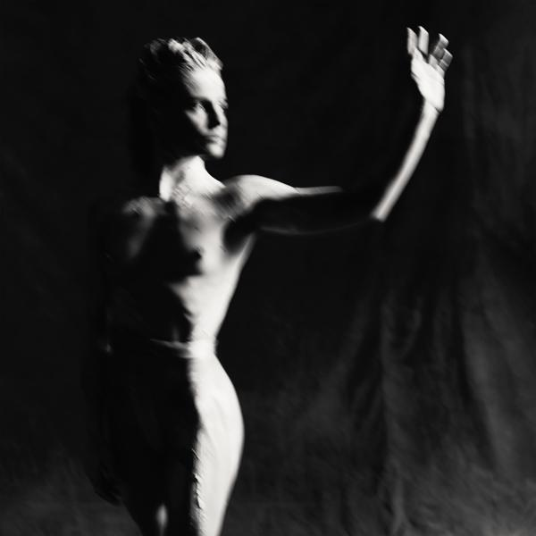 Photo en noir et blanc d'une femme en mouvement, avec un bras tendu et un effet flou.