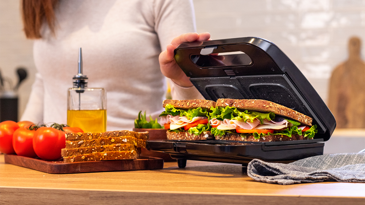 Sandwichera con sándwiches, tomates, aceite y pan.