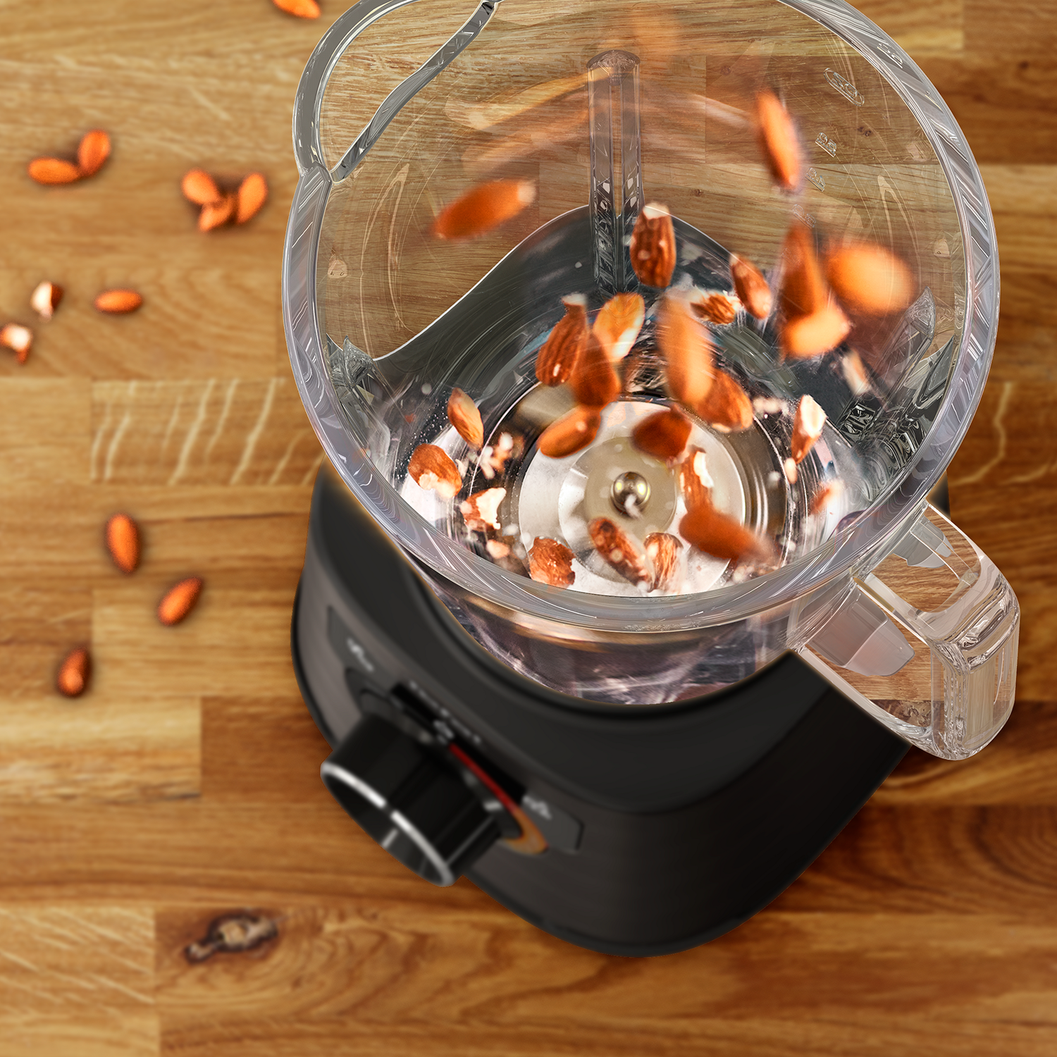 Overhead shot of a blender with almonds falling into it, on a wooden surface.