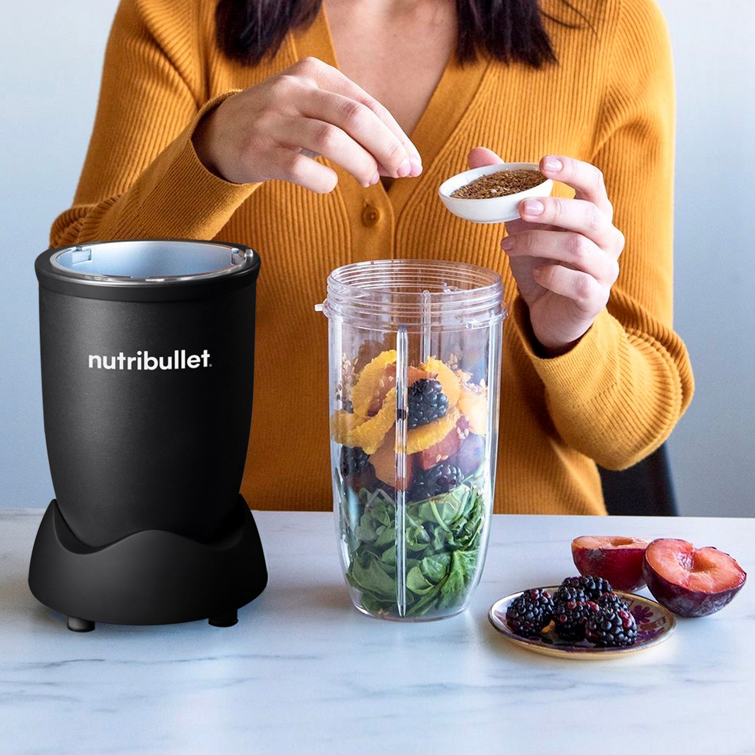Person adding seeds to a blender with fruits and vegetables.