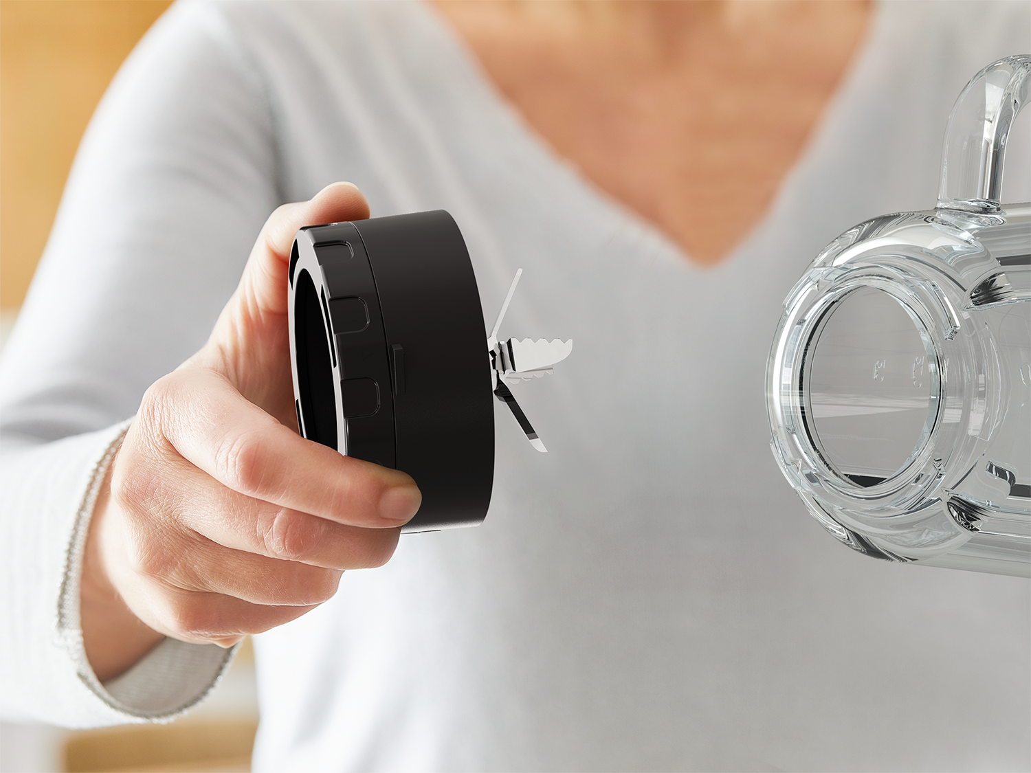 Woman holding a blender attachment with blades. The background is blurred.