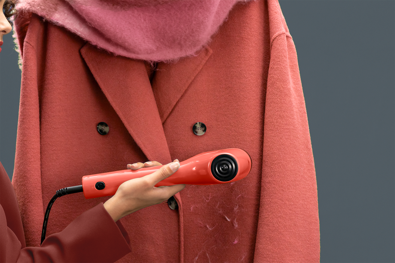 A person using a red fabric shaver on a red coat, with pink scarf.