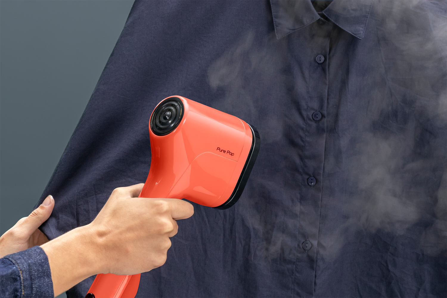 A person steaming a dark blue shirt with an orange Pure Pop steamer.