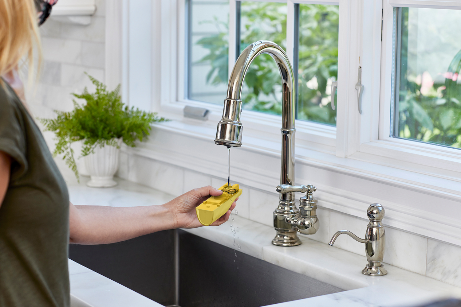 A person testing water with a yellow device at a sink.